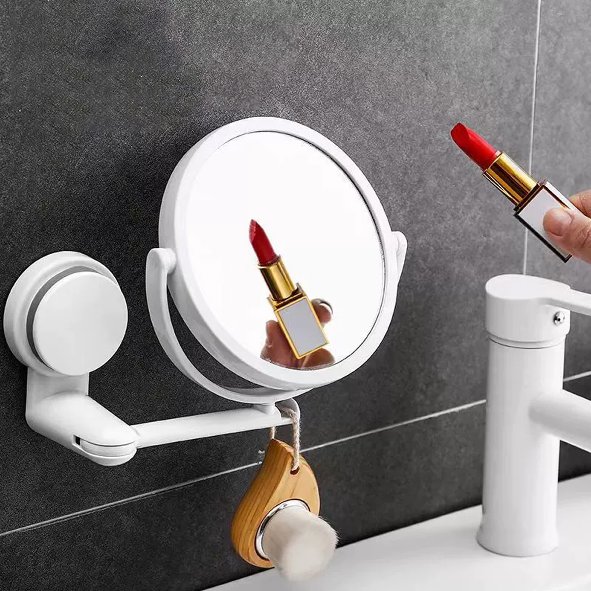 Ein weißer Spiegel reflektiert einen roten Lippenstift. Eine Person hält einen weiteren roten Lippenstift. Ein Pinsel und ein Wasserhahn sind ebenfalls sichtbar.