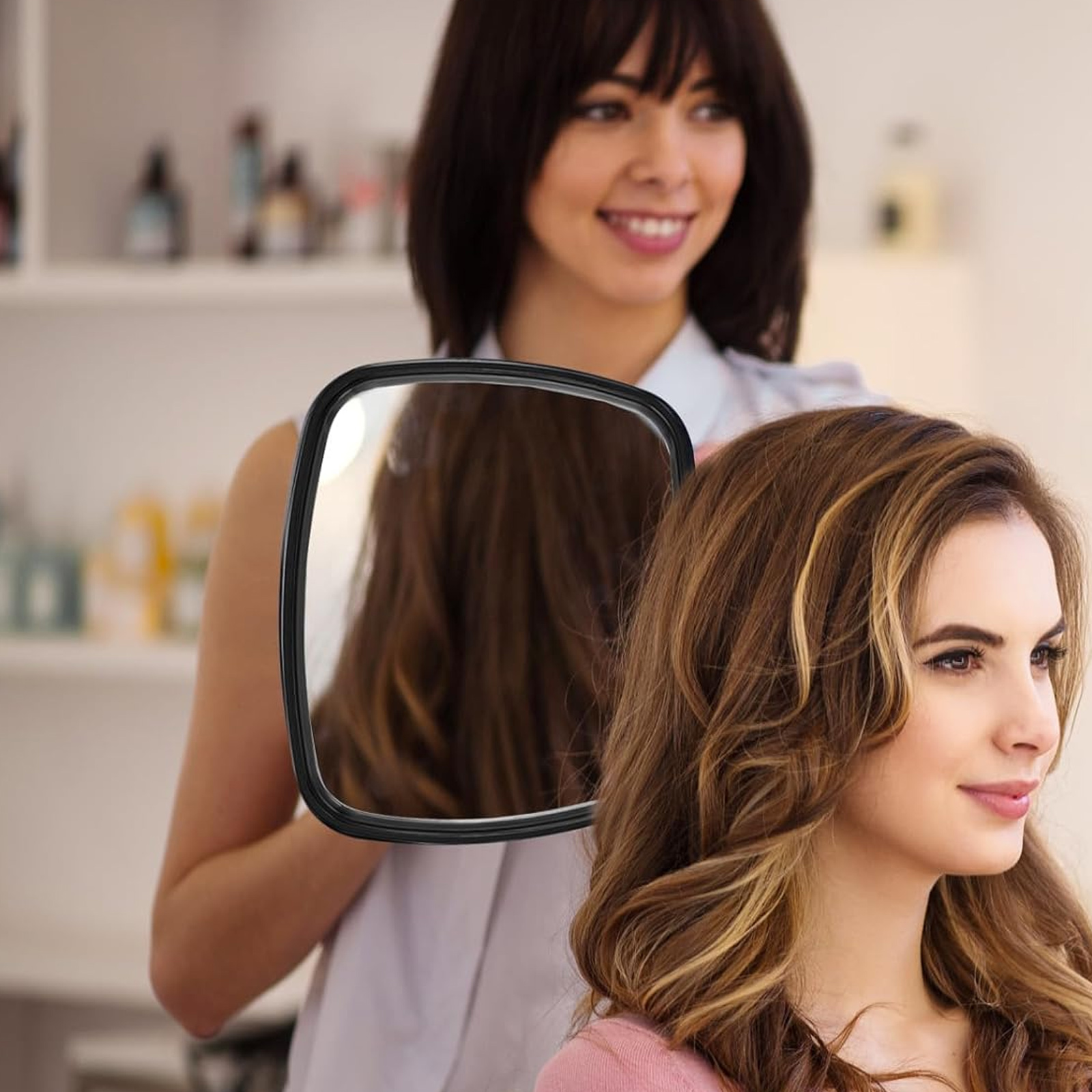 Eine Frau in einem Salon lässt sich von einer Stylistin ihre Haare im Spiegel ansehen. Die Stylistin lächelt.