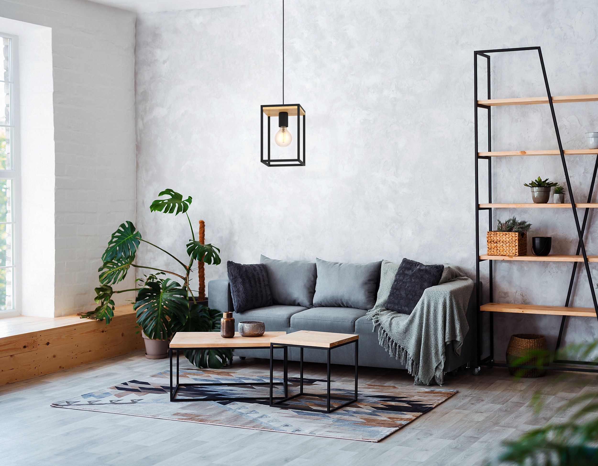 Modernes Wohnzimmer mit grauem Sofa, Holztischen, Pflanzen und einer Leuchte mit schwarzem Rahmen.