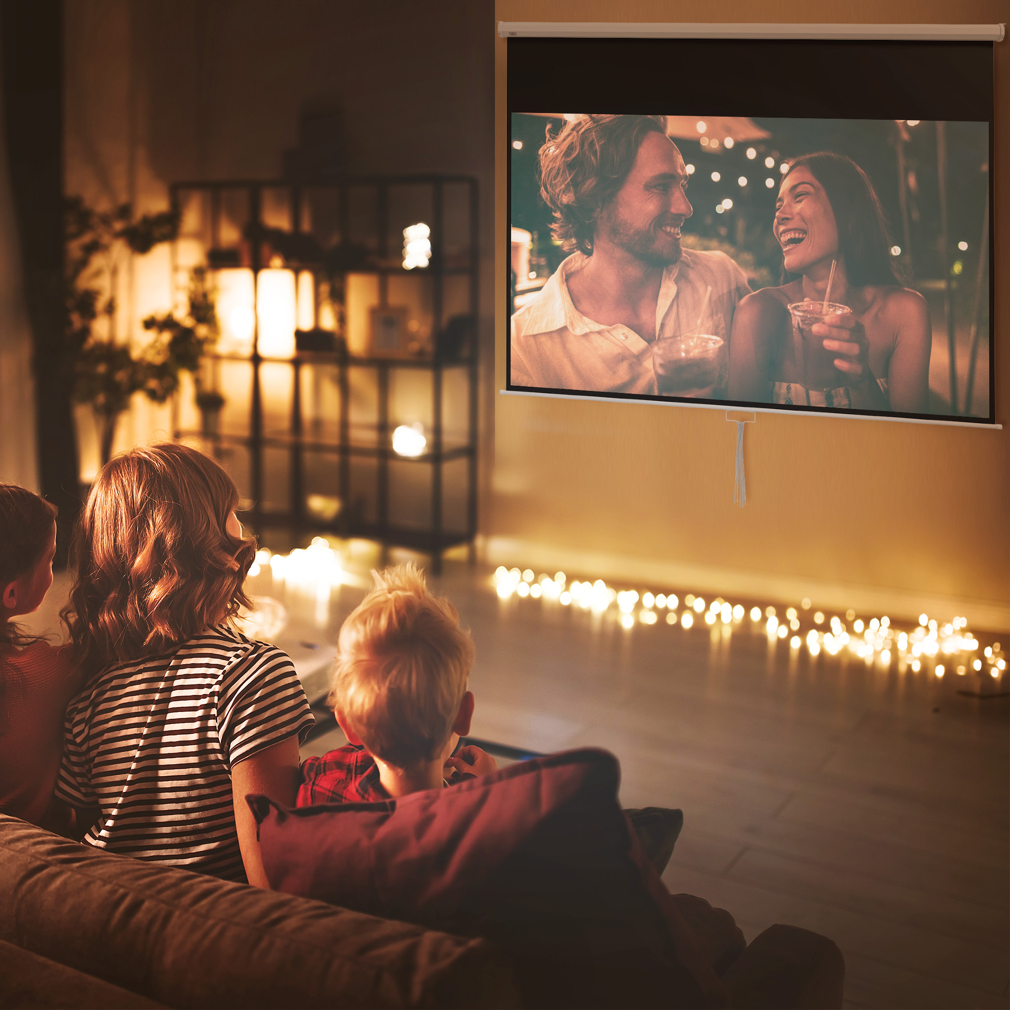 Una famiglia guarda un film proiettato su uno schermo. Il film mostra una coppia sorridente. Luci calde illuminano la stanza.