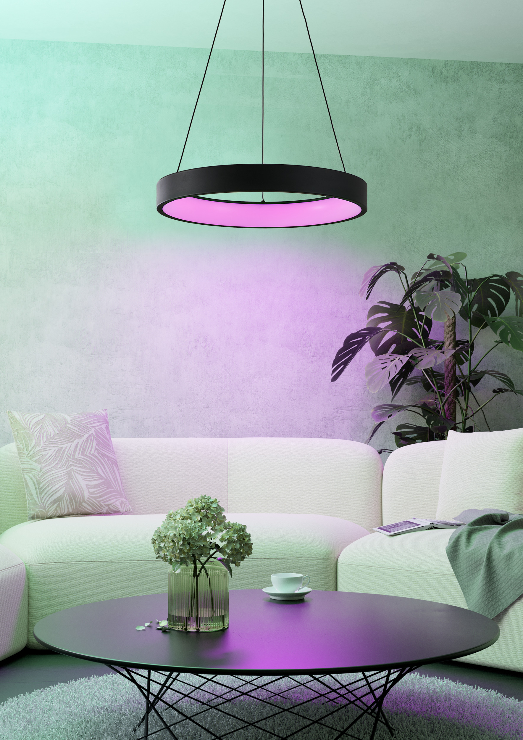 Ein modernes Wohnzimmer mit rundem schwarzem Tisch, weißem Sofa und ringförmiger Leuchte. Eine Pflanze im Hintergrund.
