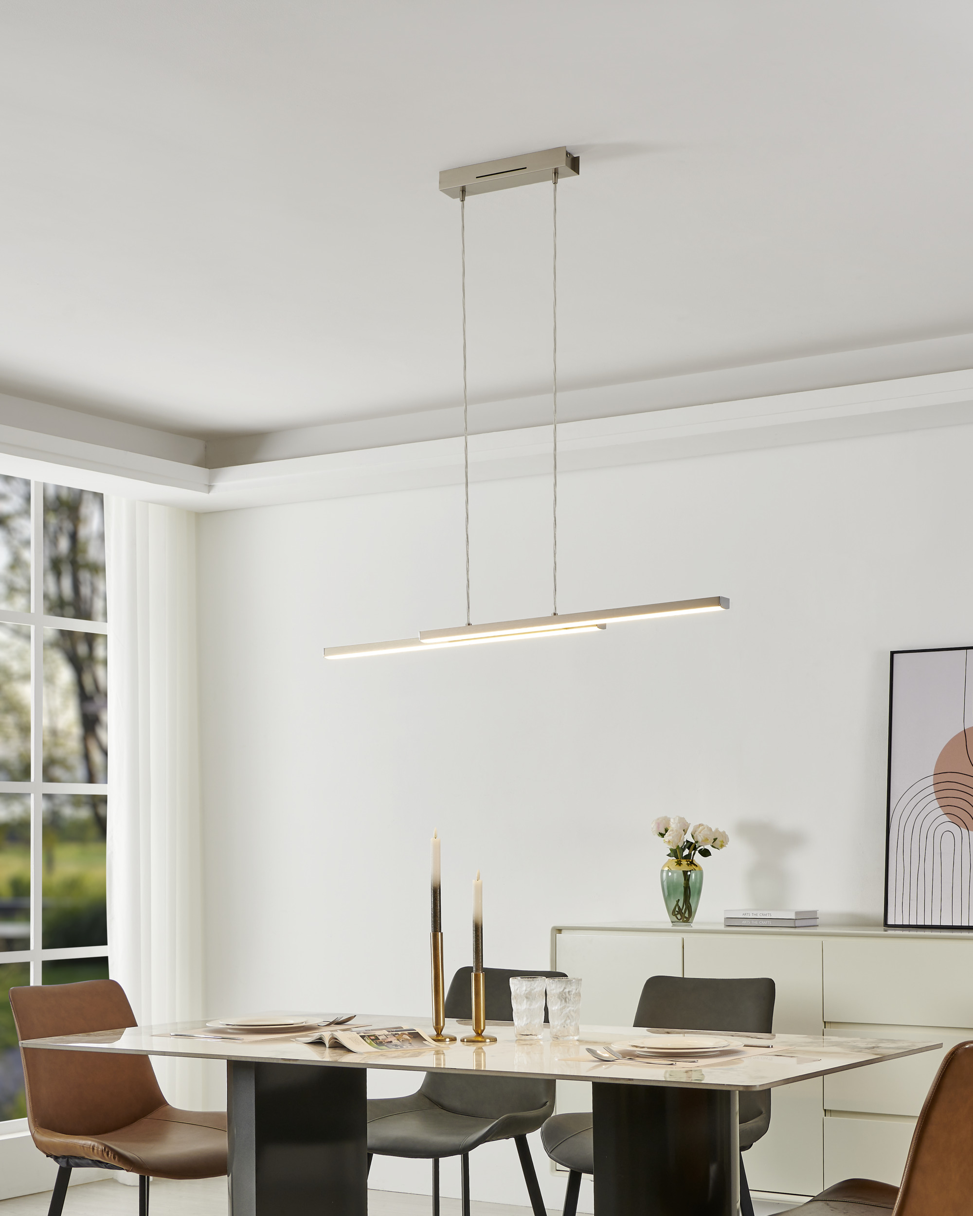 Ein Esszimmer mit Tisch, Stühlen, Kronleuchter, Kerzen und Fenster. Ein Gemälde an der Wand.
