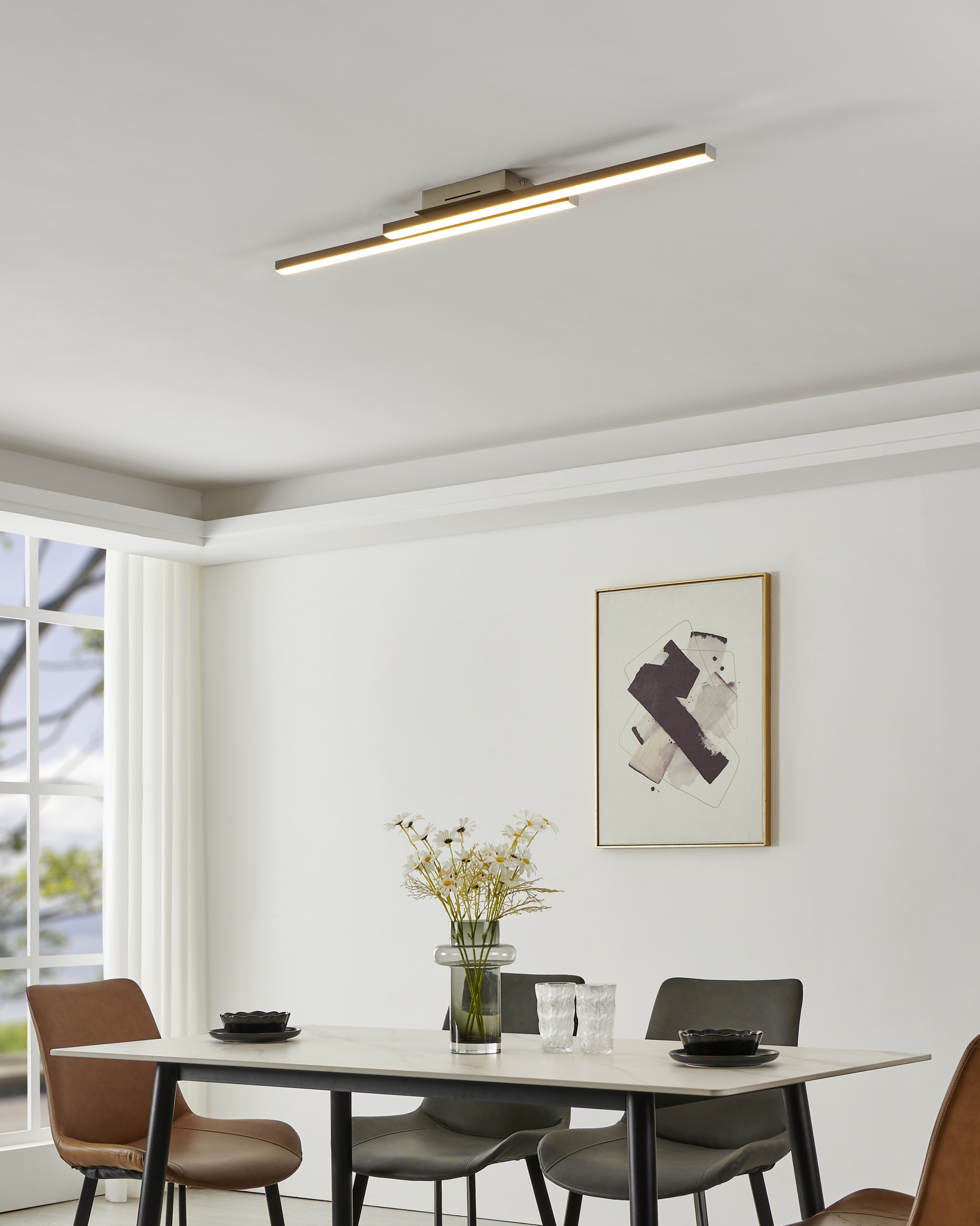 Esszimmer mit Tisch, Stühlen, Blumen und moderner Beleuchtung. Ein Gemälde an der Wand.