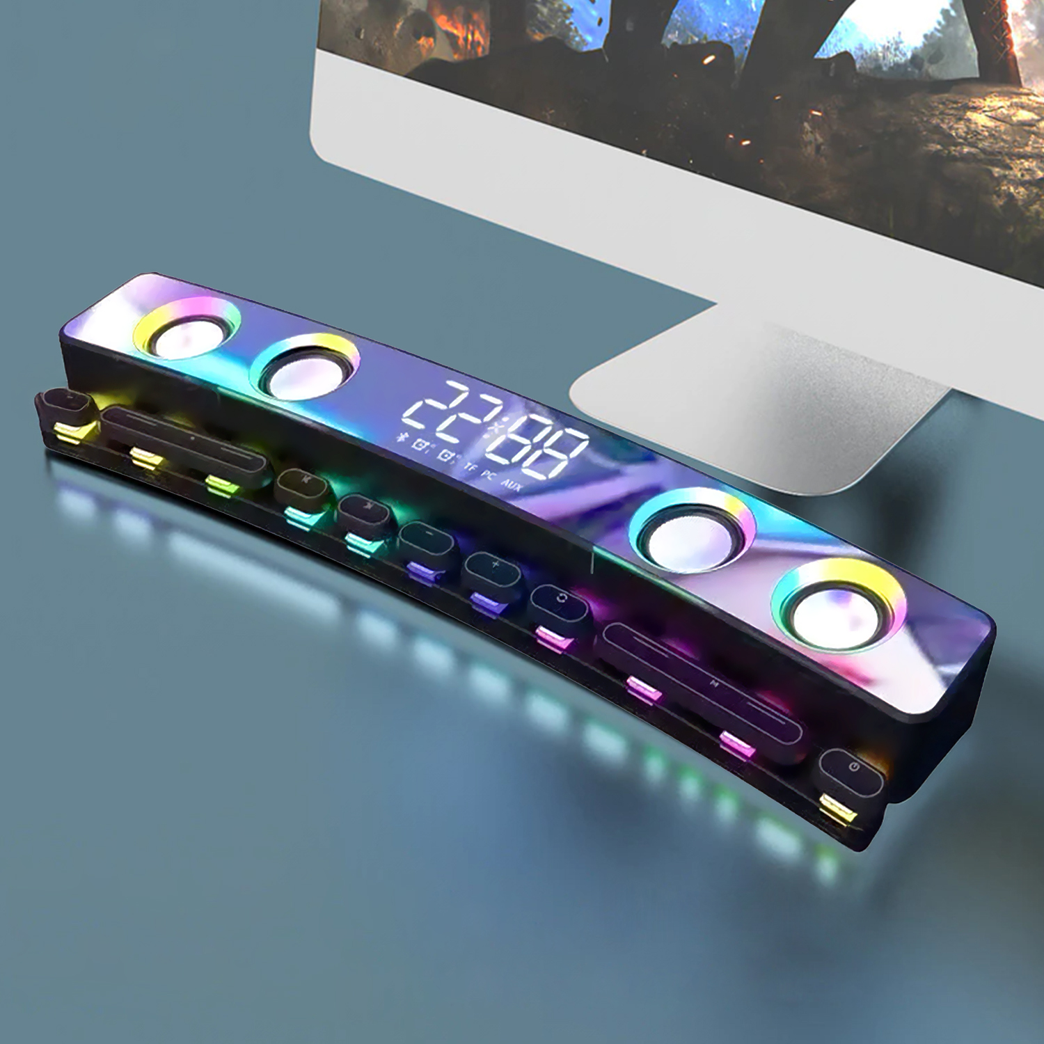 Una soundbar nera luminosa con più pulsanti e un display digitale che mostra 22:88. È su una superficie blu, vicino a un monitor del computer.