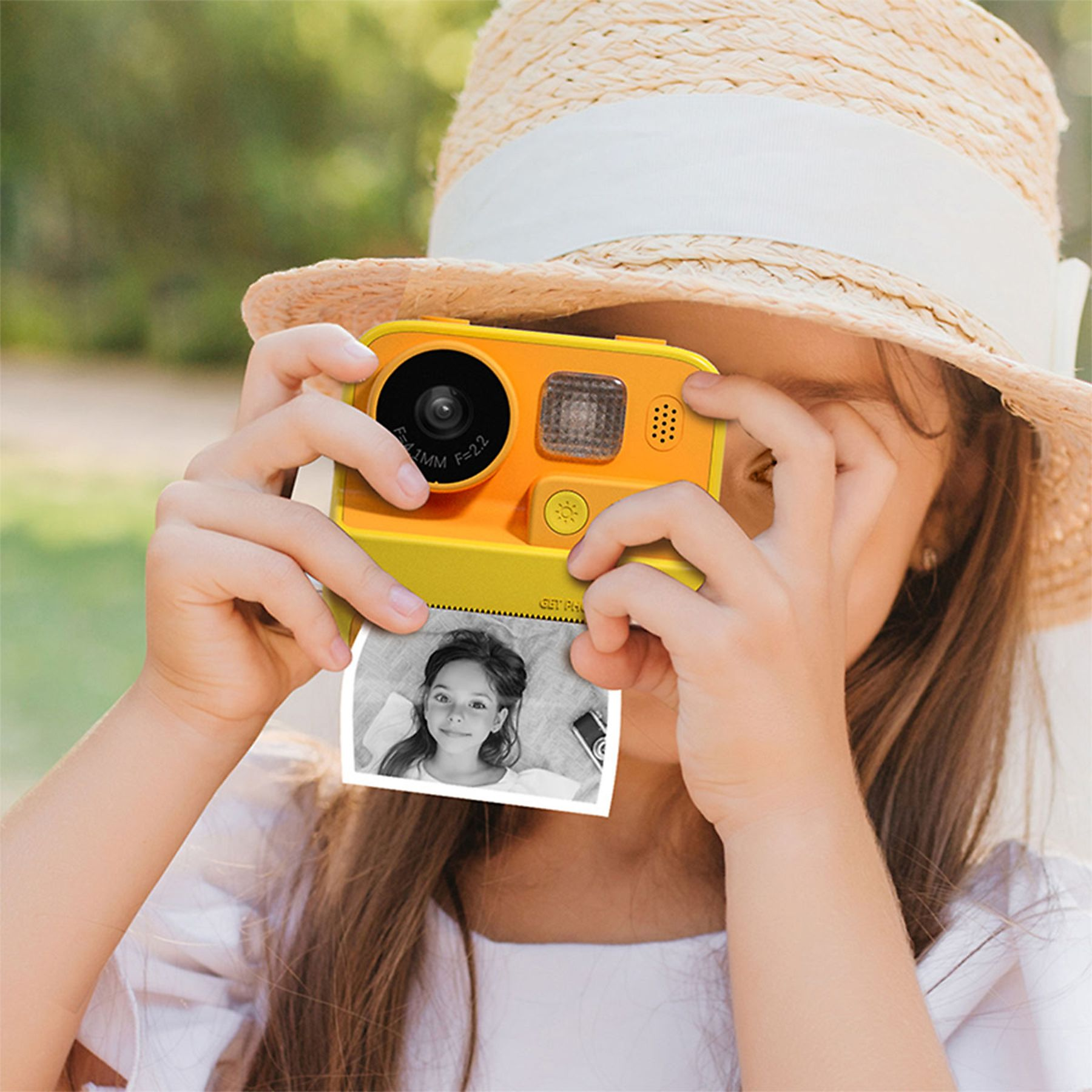 Ein Mädchen mit Strohhut macht ein Foto mit einer gelben Kamera. Ein Schwarzweißfoto ist sichtbar.