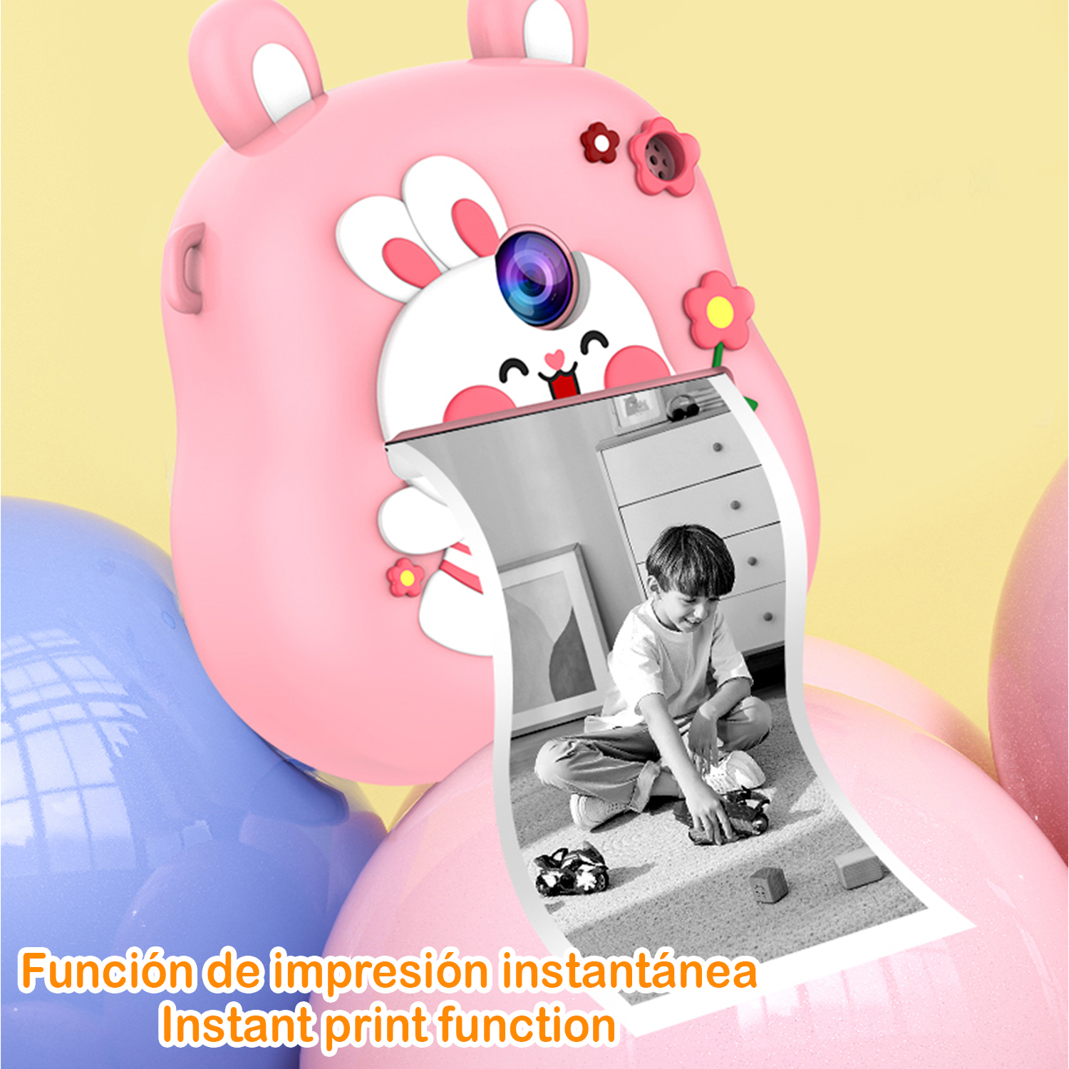 Fotocamera a stampa istantanea rosa a forma di coniglio. Un'immagine stampata mostra un bambino che gioca con macchinine. Testo: Funzione di stampa istantanea.