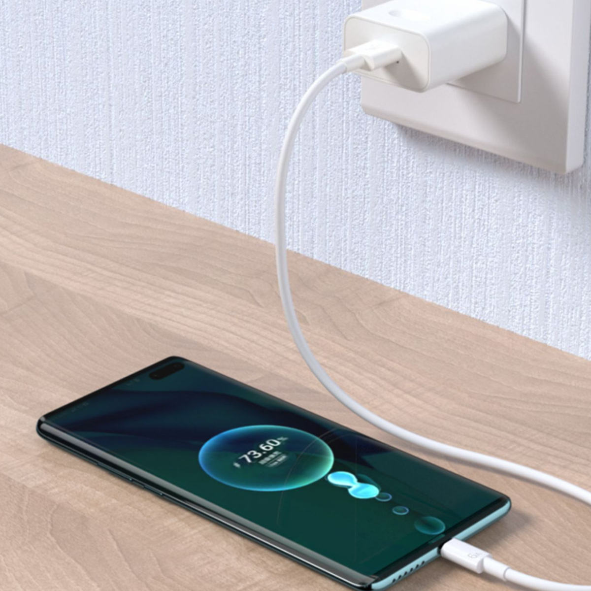 Ein Telefon, das auf einer Holzoberfläche aufgeladen wird. Ein Ladegerät ist an der Wand eingesteckt und mit dem Telefon verbunden, das 73,60 % Ladung anzeigt.