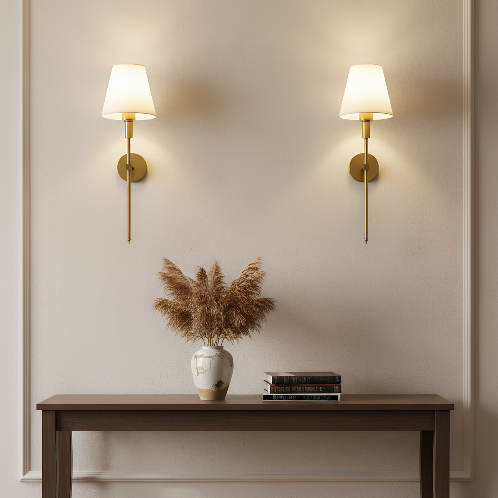 Zwei Wandleuchten flankieren eine Vase mit Pampasgras und Büchern auf einem Tisch. Die Wand ist beige.