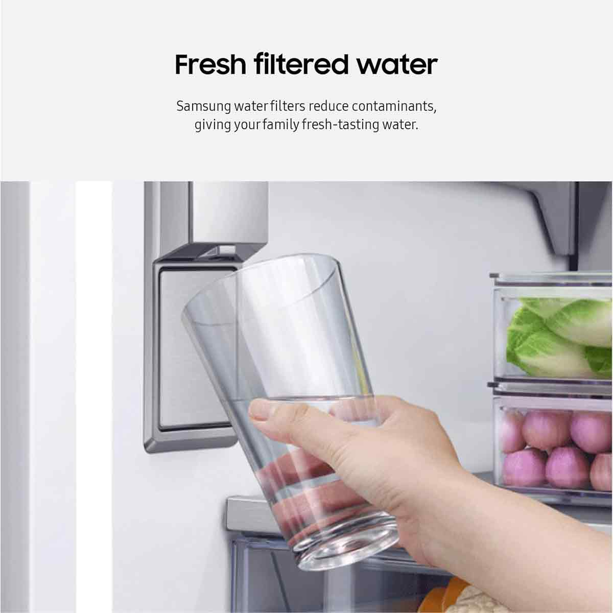 Eine Hand hält ein Glas Wasser aus einem Kühlschrankspender. Gemüse in durchsichtigen Behältern im Hintergrund.