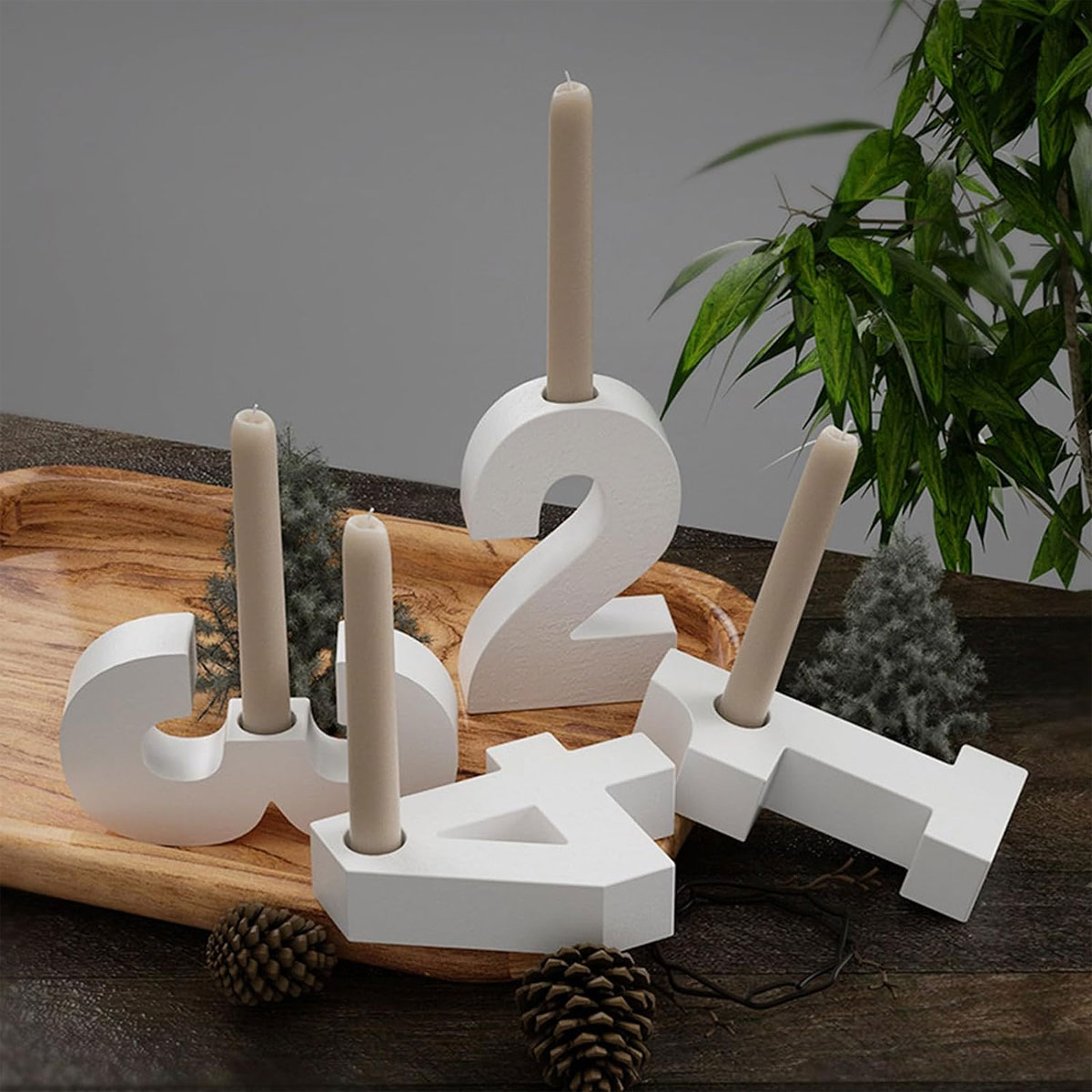 Weiße Zahlenkerzen 1,2,3,4 mit beigefarbenen Kerzen auf einem Holztablett mit Tannenzapfen und grünen Pflanzen im Hintergrund.