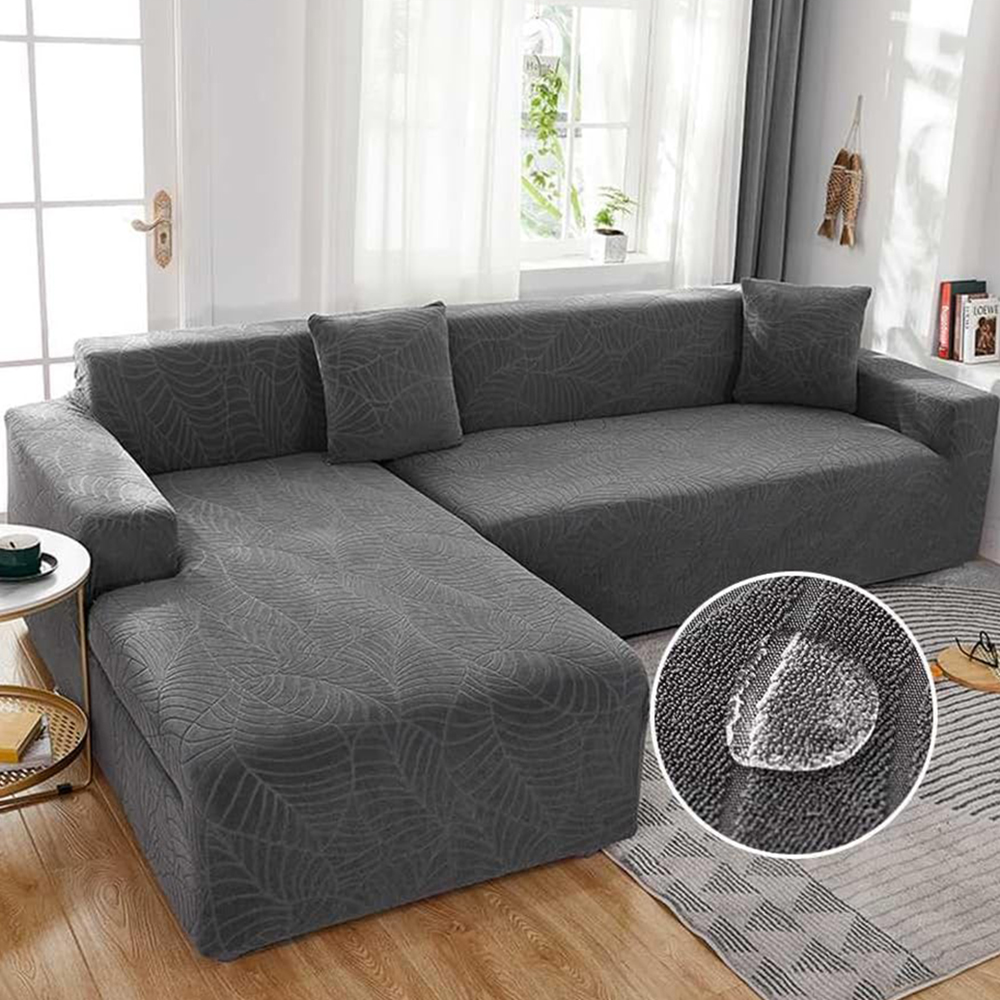 Graues L-förmiges Sofa mit Blattmuster, zwei Kissen, einem Beistelltisch und einem Fenster im Hintergrund. Ein Wassertropfen ist zu sehen.