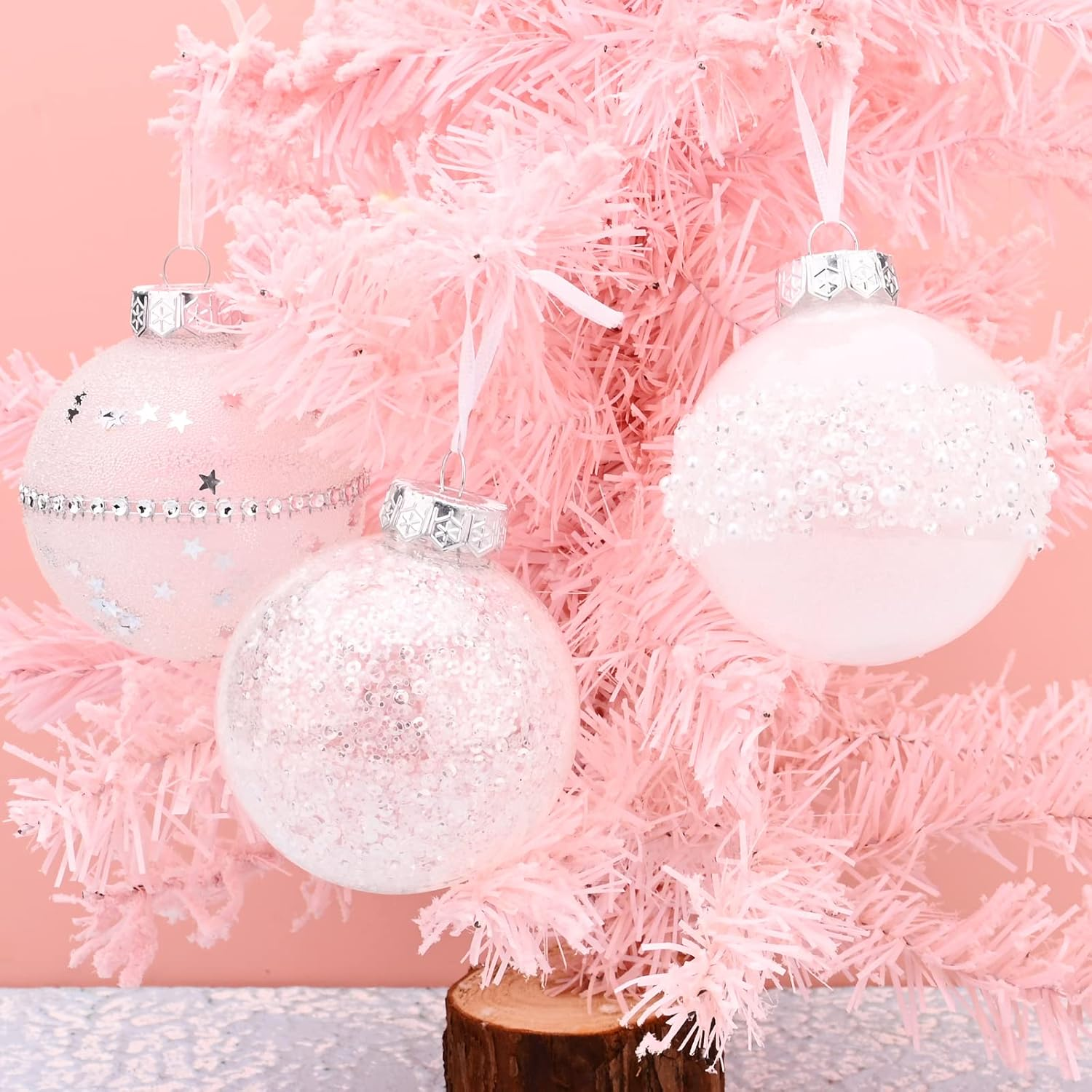 Drei rosa Weihnachtskugeln hängen an einem kleinen rosa Baum. Die Ornamente sind mit Sternen, Pailletten und Perlen verziert.