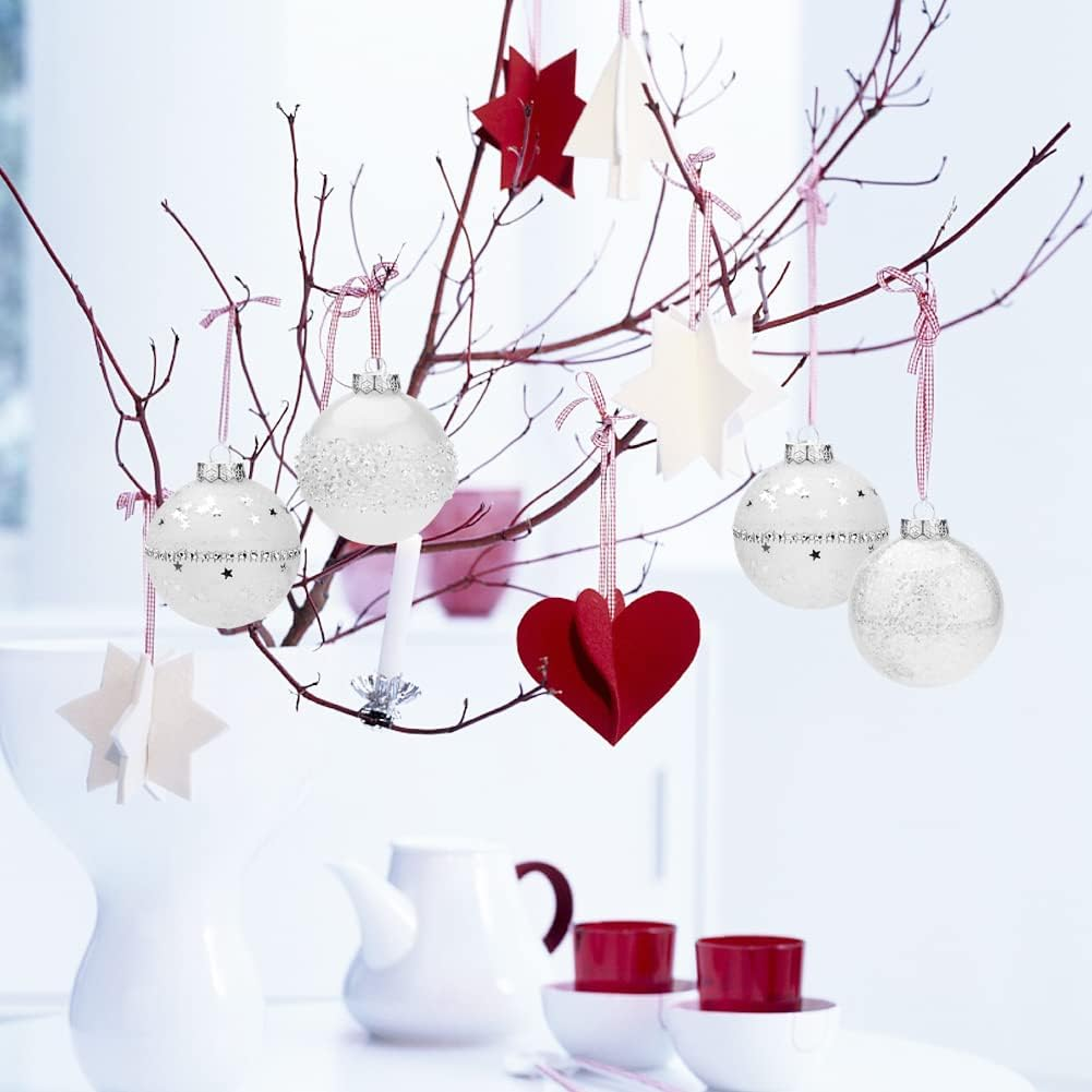 Weihnachtsschmuck, Sterne und ein Herz hängen an Ästen. Weiße Teekanne, Tassen und eine Vase stehen auf einem Tisch in hellem Raum.