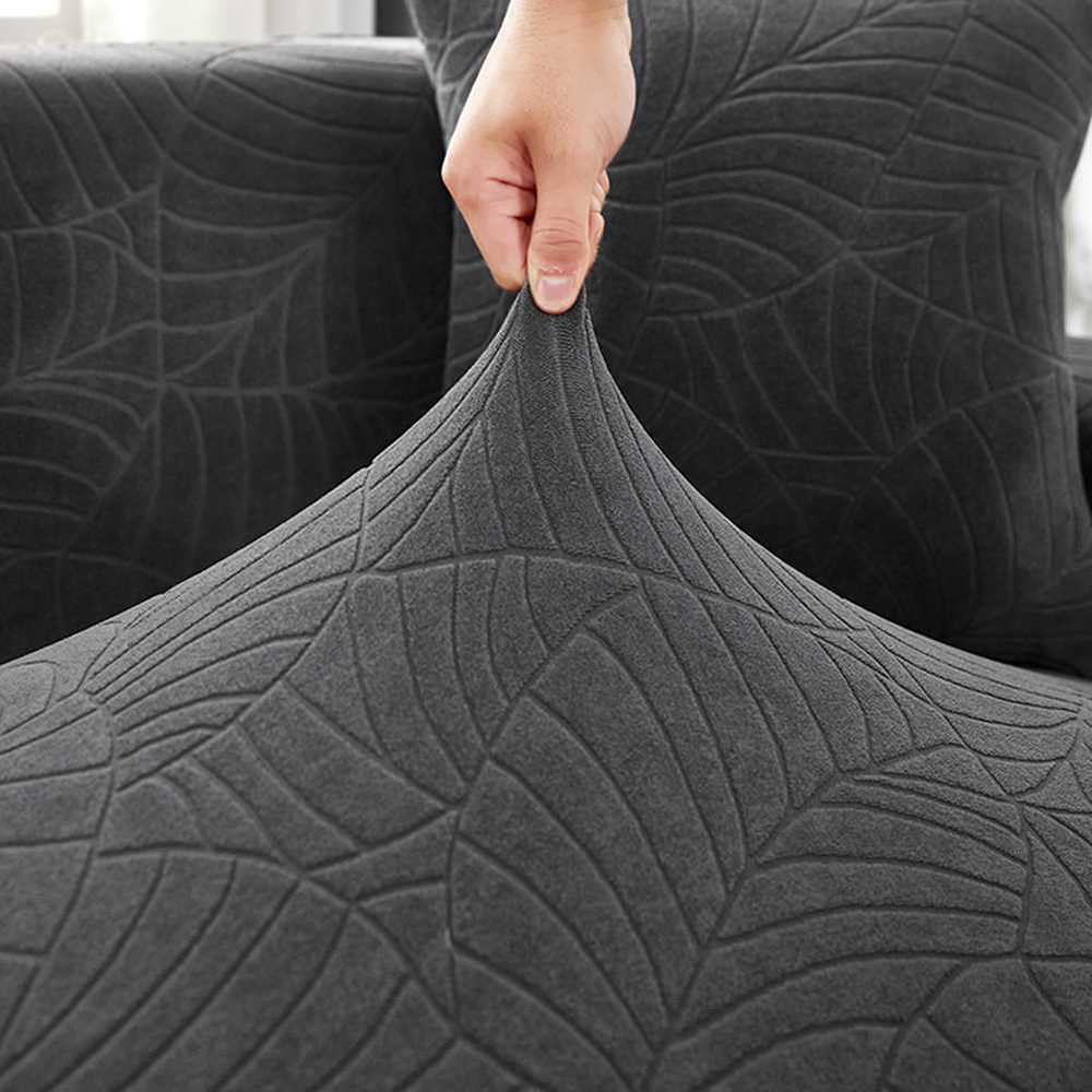 Eine Hand zieht eine graue Sofahusse hoch. Die Hülle hat ein Blättermuster. Der Hintergrund zeigt mehr von dem Sofa.
