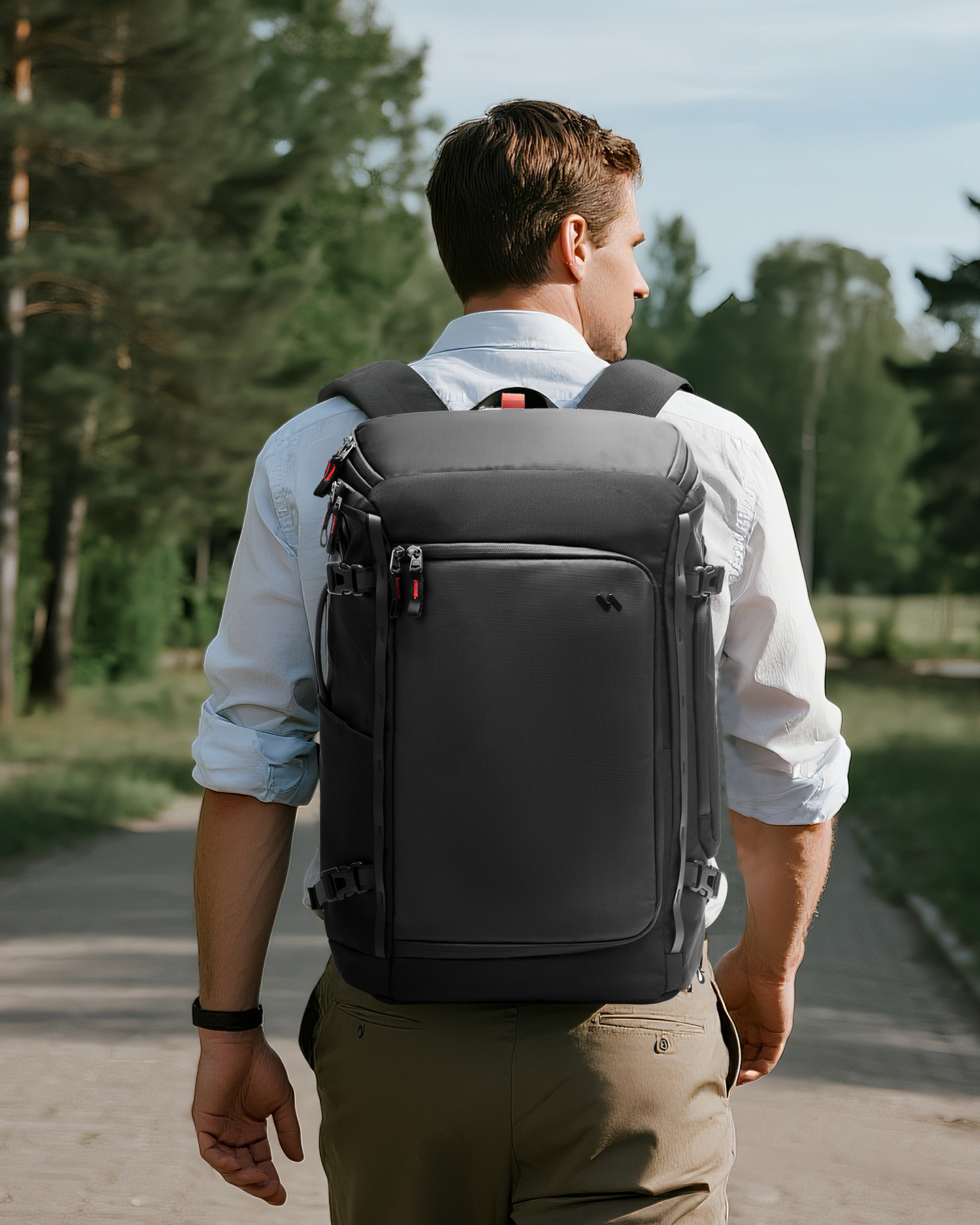 Ein Mann geht weg von der Kamera und trägt einen schwarzen Rucksack. Er befindet sich auf einem Weg mit Bäumen im Hintergrund.