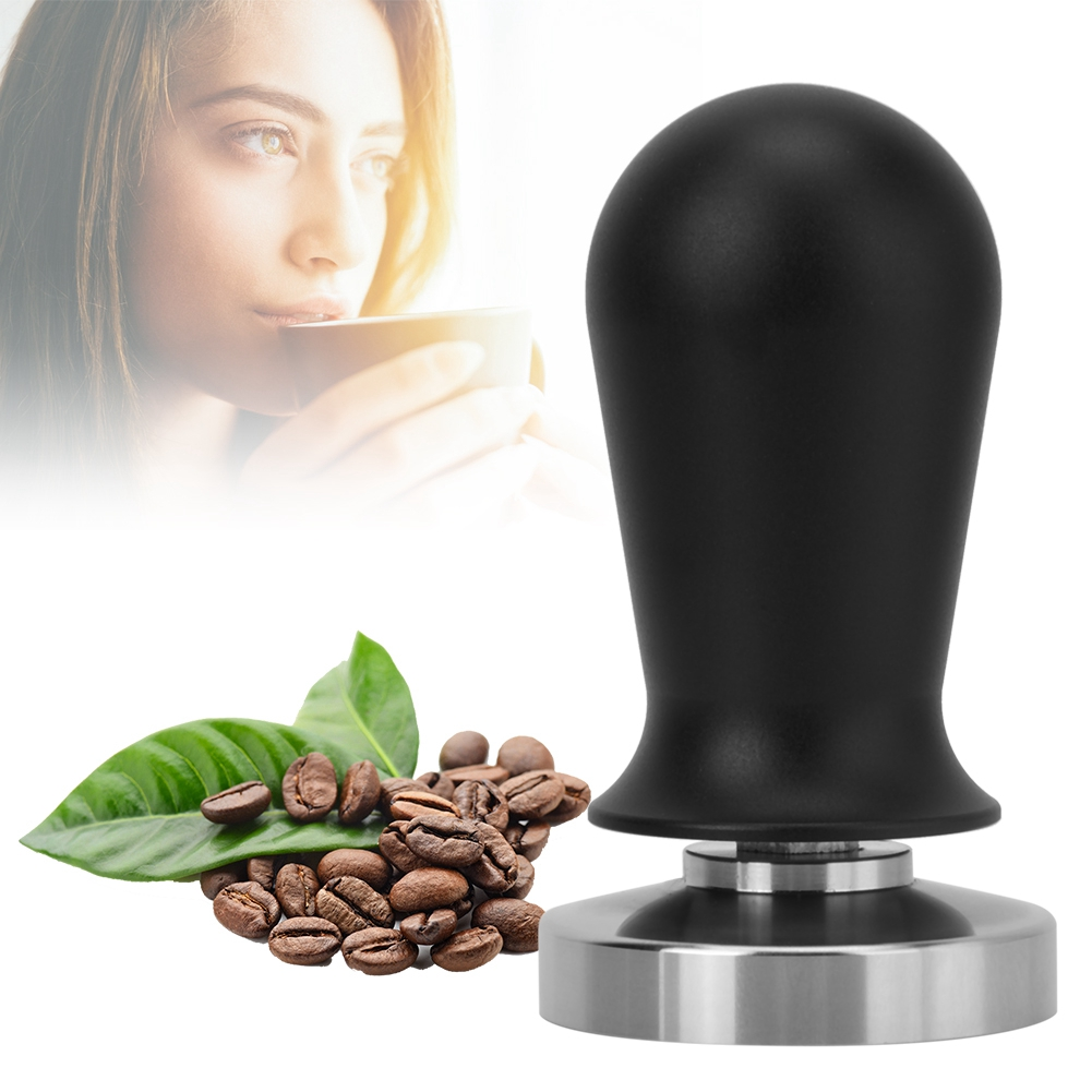 Eine Frau, die Kaffee trinkt, Bohnen, Blätter und ein schwarzer Tamper. Der Tamper hat eine silberne Basis.