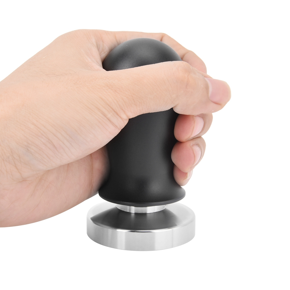Eine Hand hält einen schwarzen Kaffeestampfer. Der Stampfer hat einen schwarzen Griff und eine silberne Basis. Der Hintergrund ist weiß.