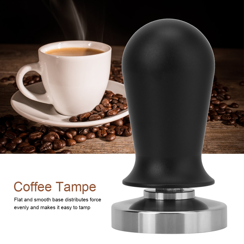 Ein Kaffee-Tamper mit schwarzem Griff und silberner Basis, eine Tasse Kaffee und Kaffeebohnen auf einem Holztisch.