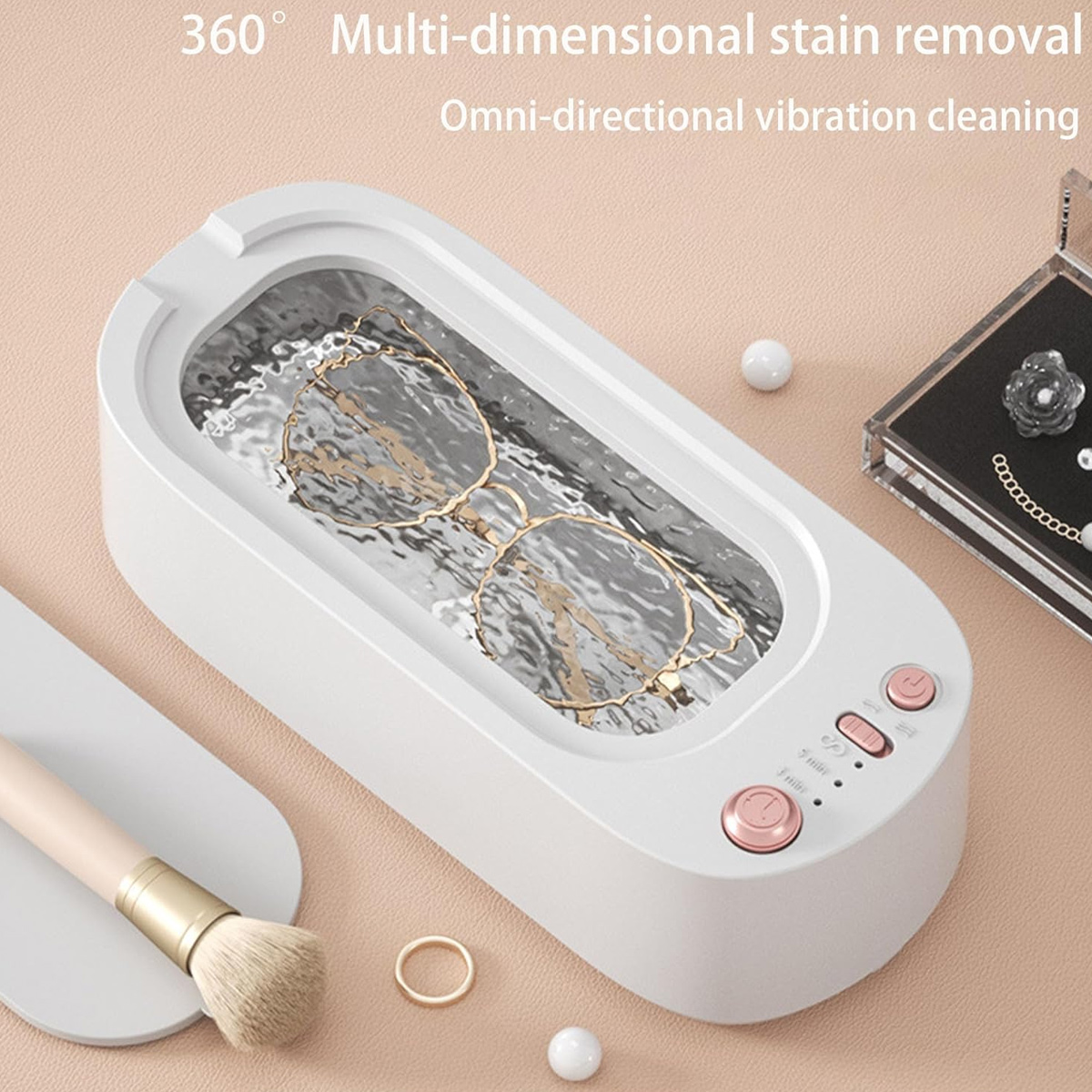 Ein weißer Ultraschallreiniger mit Brille. Ein Make-up-Pinsel, eine Schmuckschatulle und ein Ring sind in der Nähe. Rosafarbene Knöpfe sind am Reiniger.
