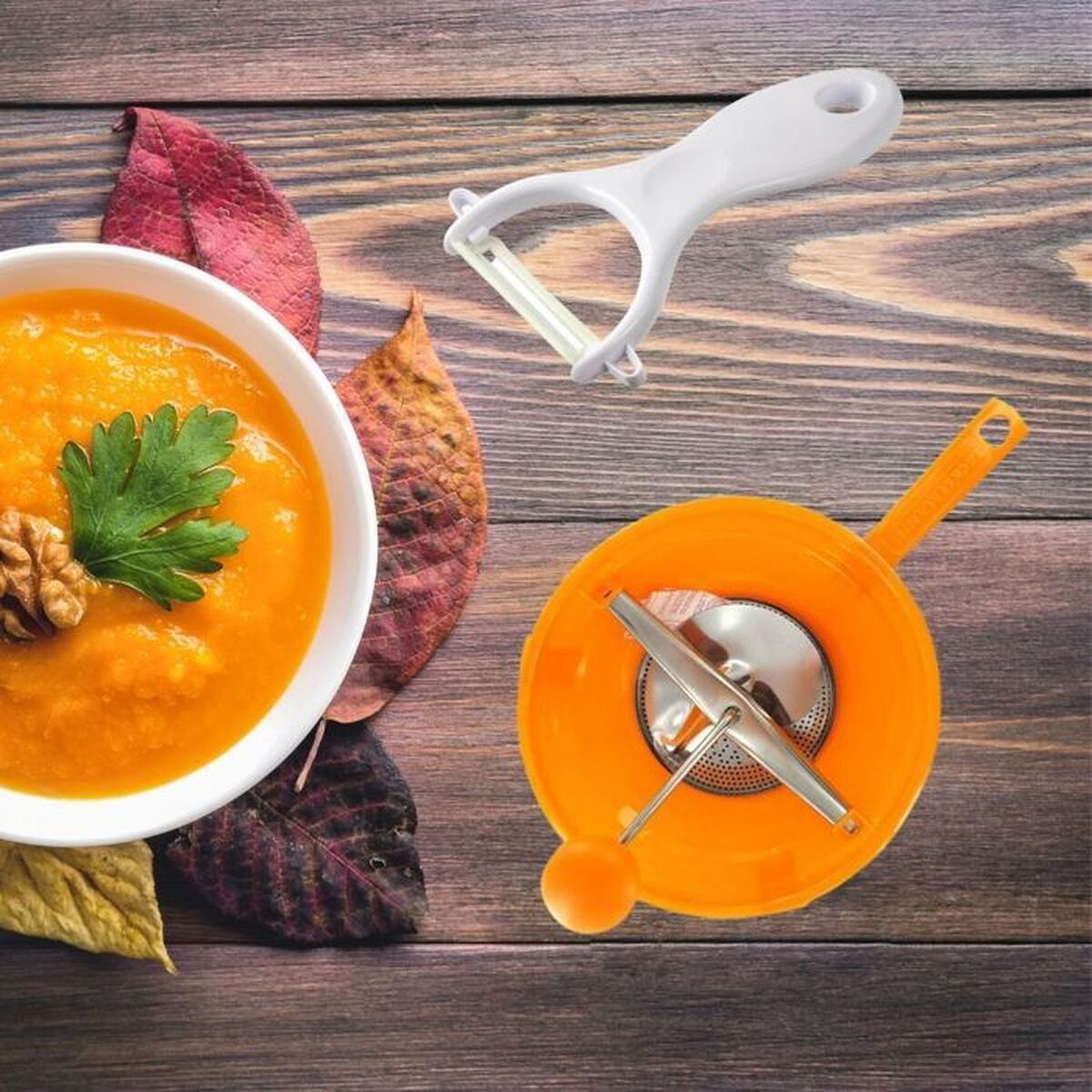 Eine Schüssel Suppe mit Walnuss und Petersilie, ein Schäler und eine Flotte auf einem Holztisch mit Herbstblättern.