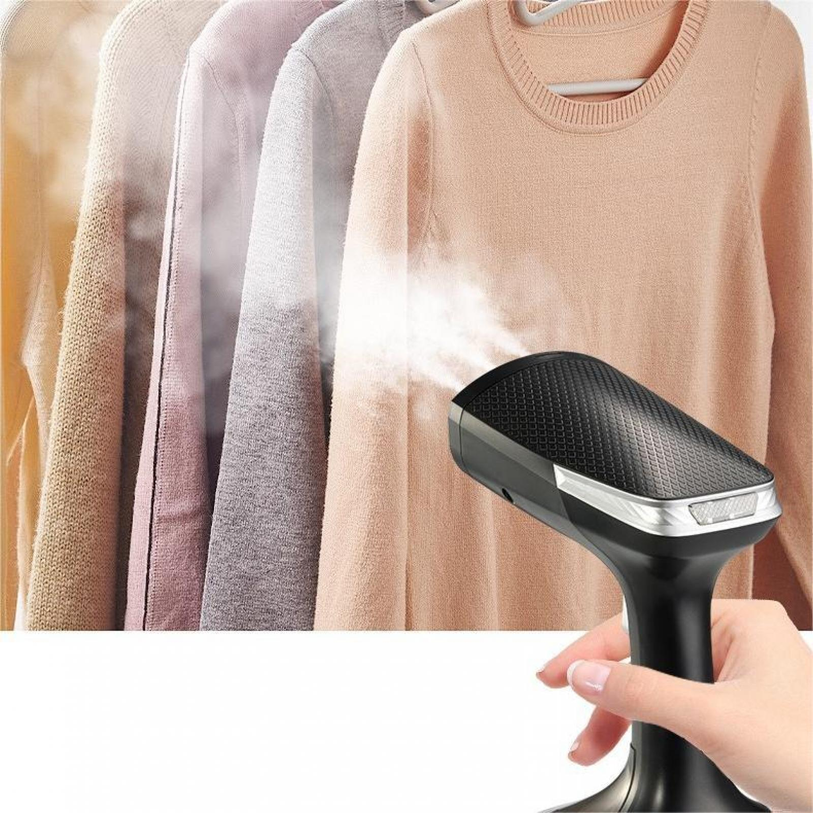 Eine Hand dämpft einen Pullover. Andere Pullover hängen im Hintergrund.
