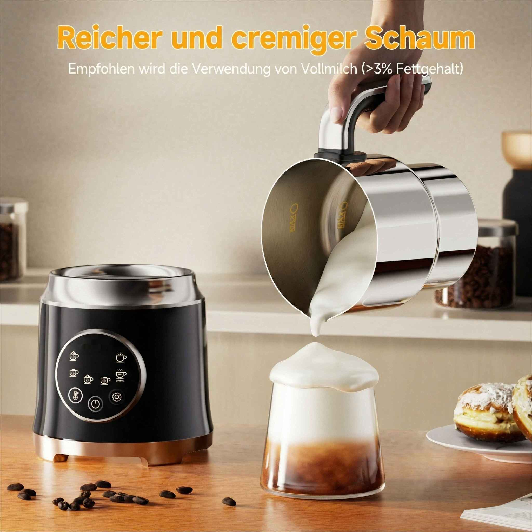 Eine Person gießt Milchschaum in ein Glas. Links ist ein schwarzer Milchaufschäumer. Donuts sind im Hintergrund auf einem Teller.
