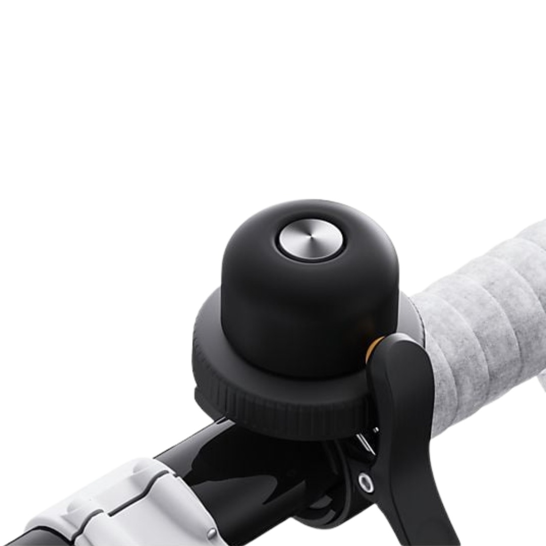 Close-up van een zwarte fietsbel met een zilveren bovenkant. Grijs stuurlint is zichtbaar. Zwarte en witte fietsonderdelen zijn aanwezig.