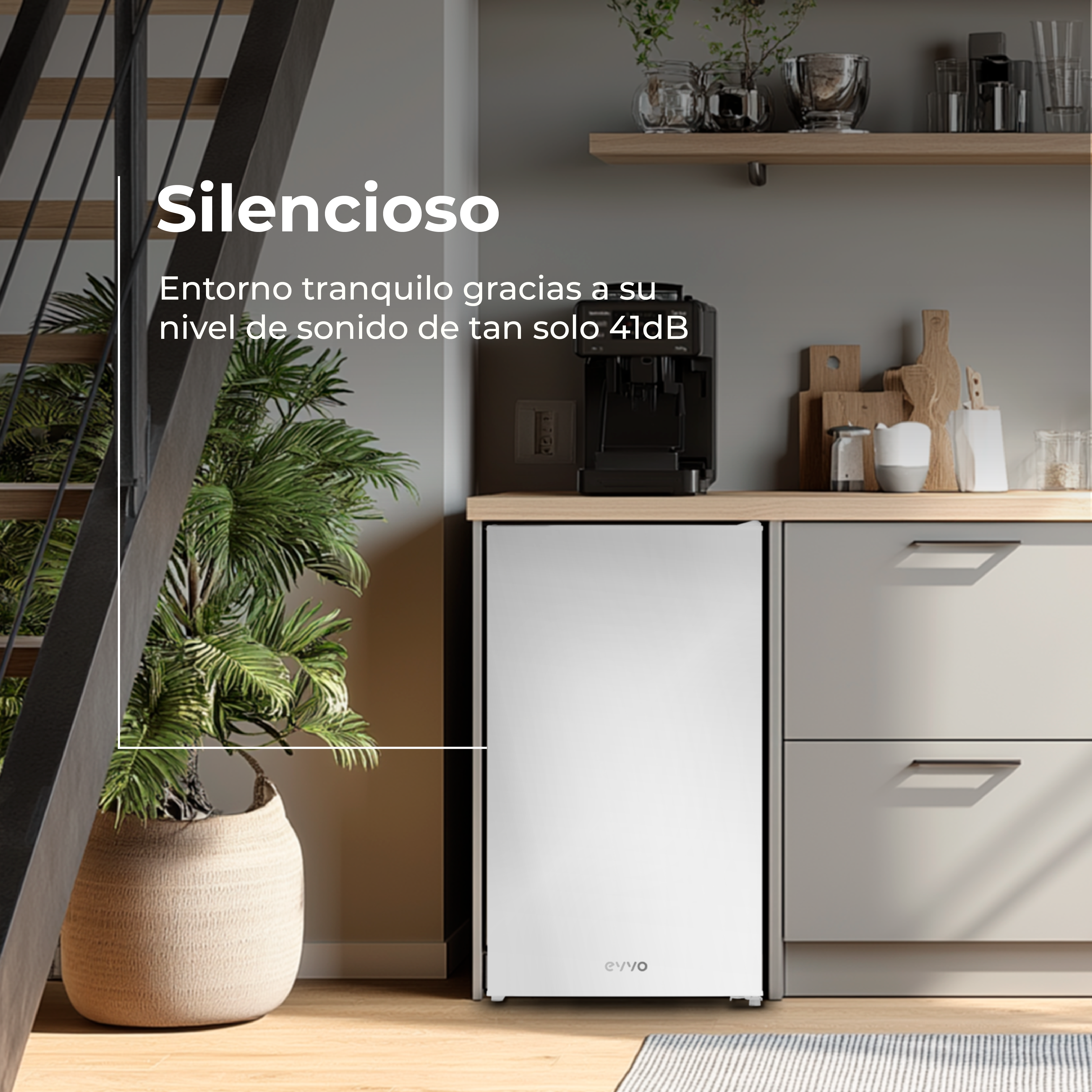 Un refrigerador blanco en una cocina. Una planta en maceta está en primer plano. Escaleras visibles en el fondo.