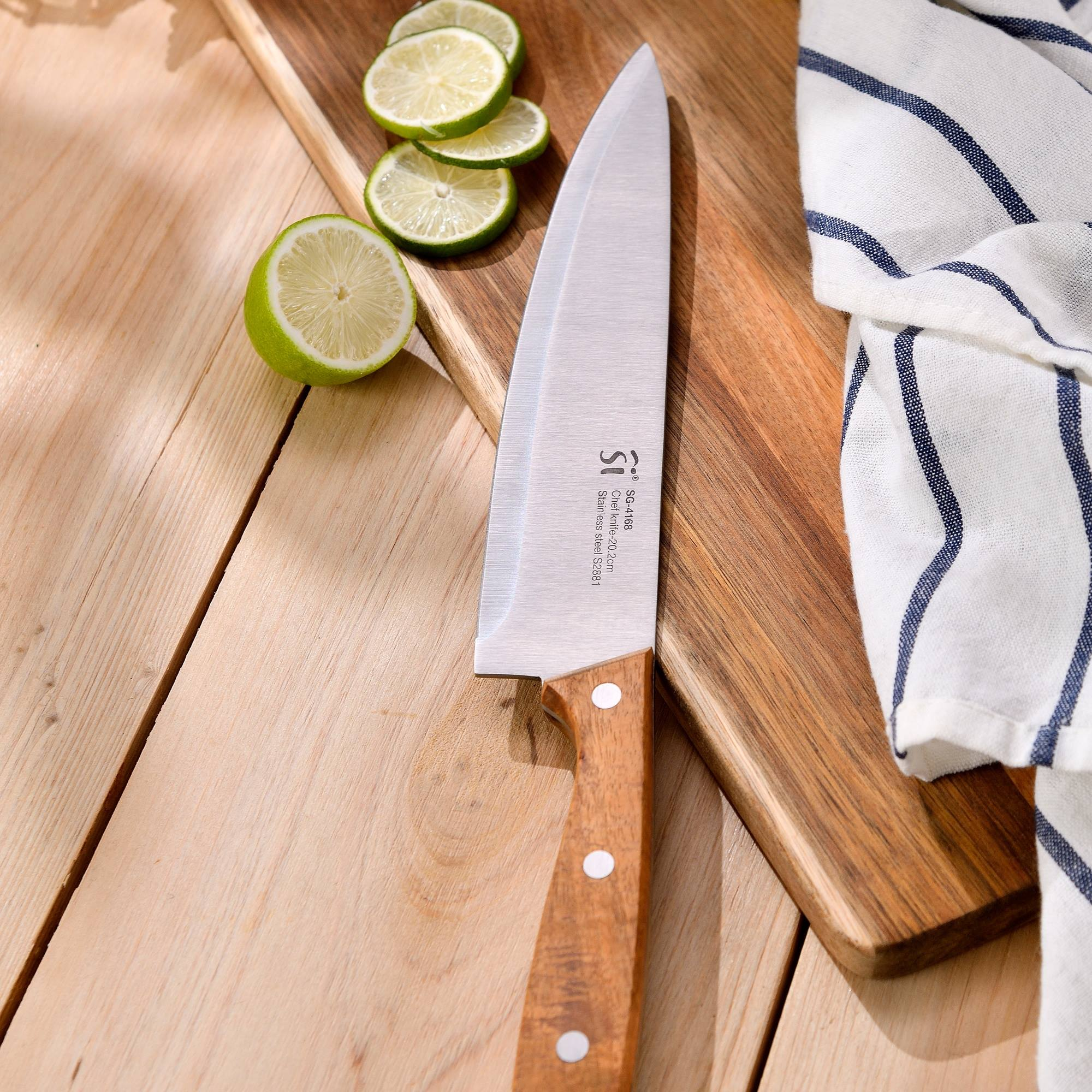 Un cuchillo de chef sobre una tabla de madera con rodajas de lima y un paño a rayas blancas y azules.