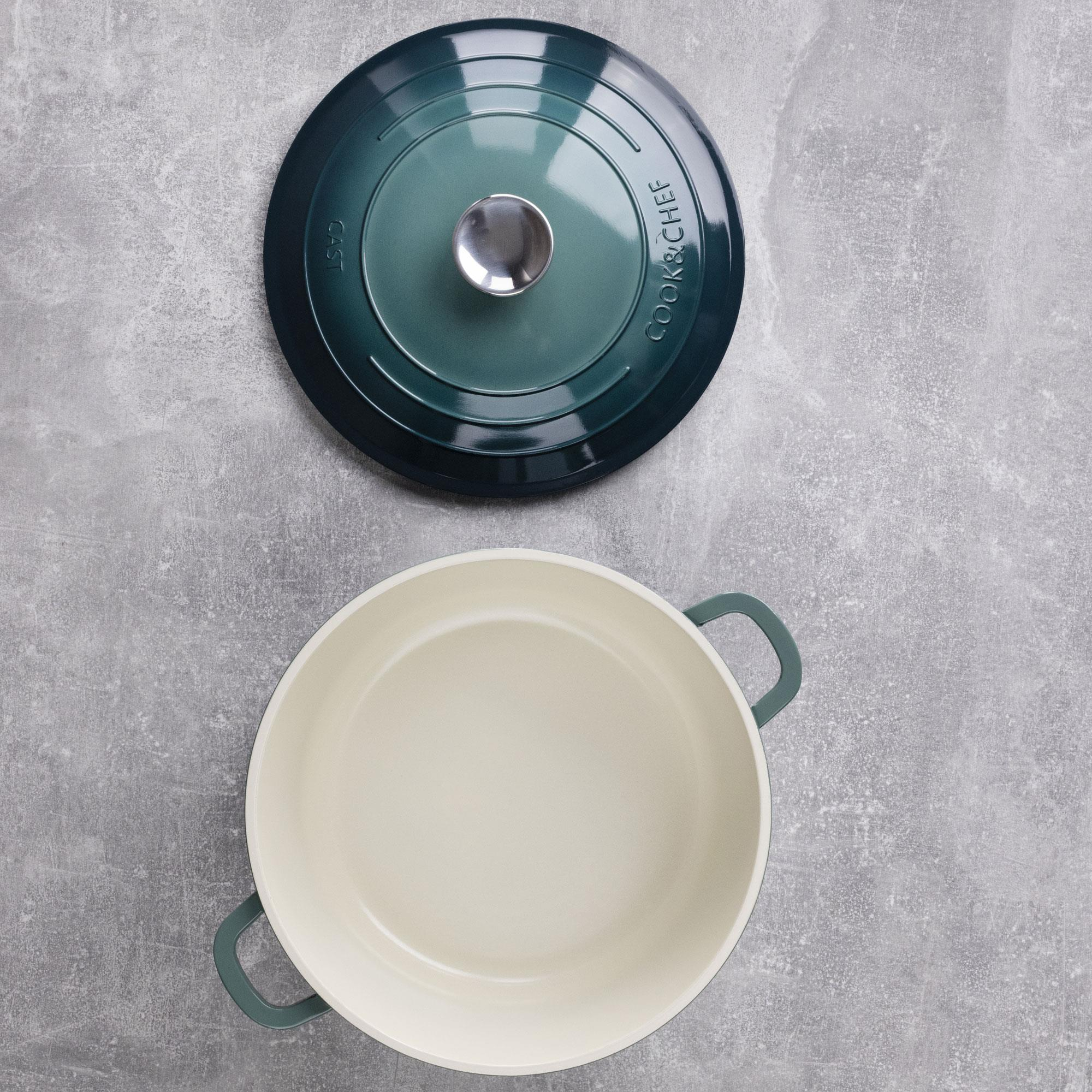 Una olla verde azulado con tapa a un lado, sobre una superficie gris texturizada. La olla está vacía.