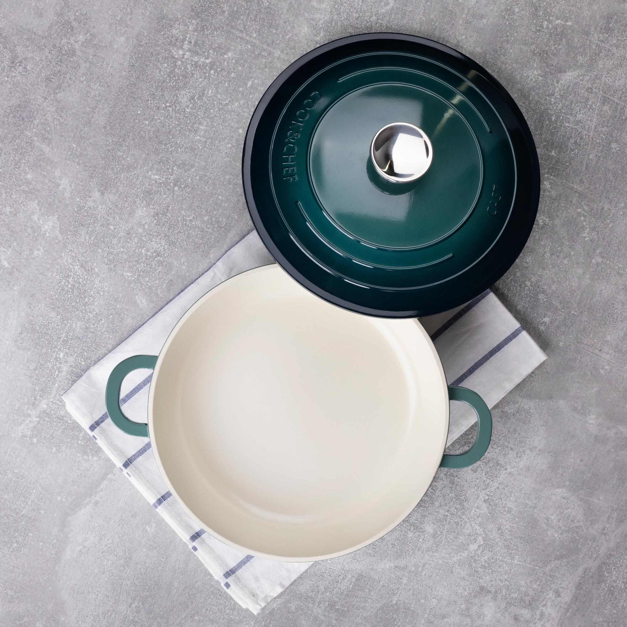 Toma cenital de una olla verde azulado con tapa quitada sobre un paño estampado sobre una superficie gris.