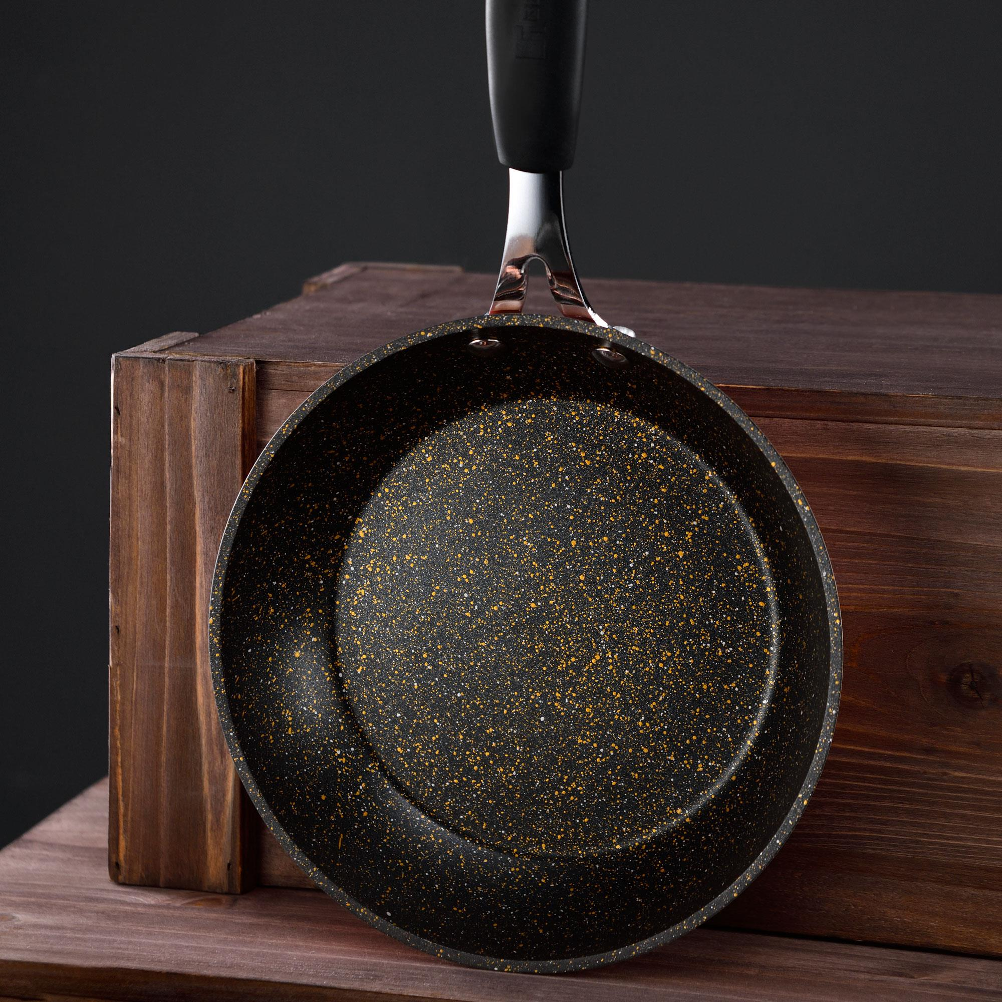 Una sartén con mango negro sobre una caja de madera. La sartén tiene un diseño moteado.
