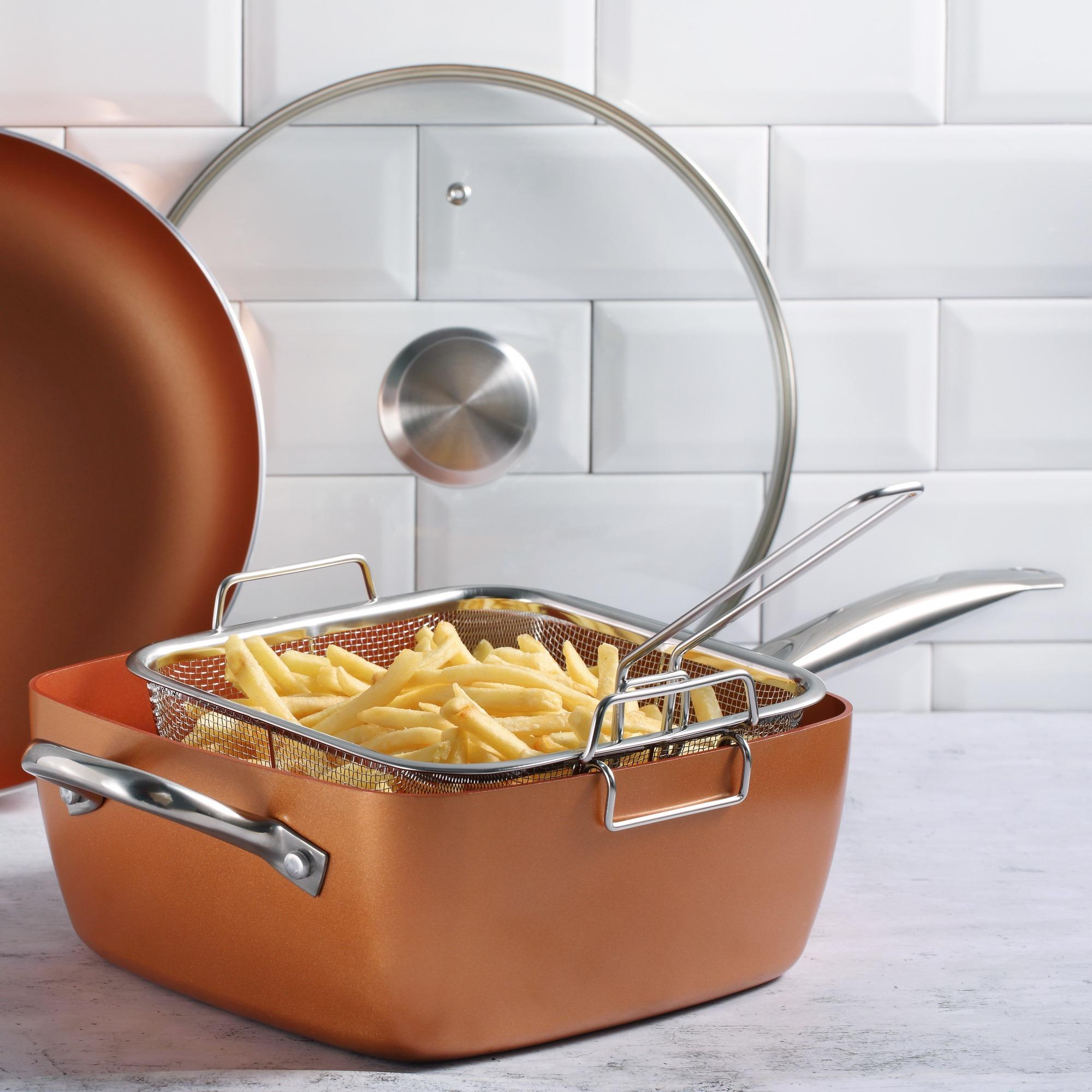 Sartén de color cobre con cesta de patatas fritas. También hay una tapa de cristal y un fondo de azulejos blancos.