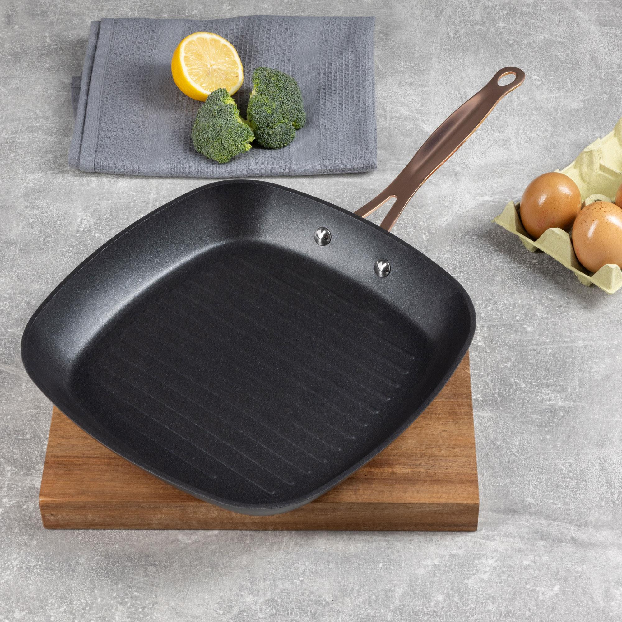 Una sartén para asar a la parrilla sobre madera, con brócoli, limón, huevos y un paño gris. Mango de cobre en la sartén.