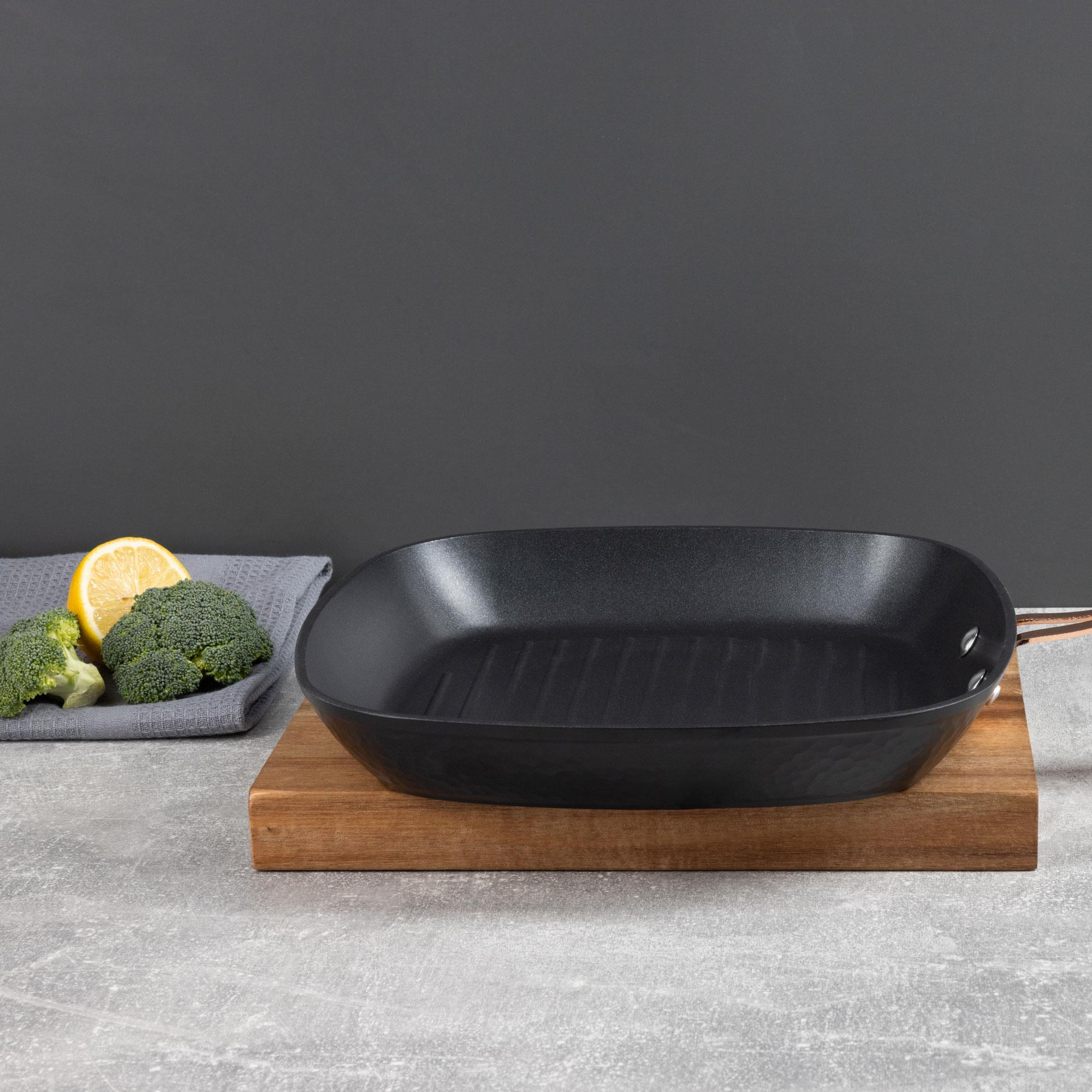 Sartén de parrilla negra sobre tabla de madera con brócoli y limón. Fondo gris.