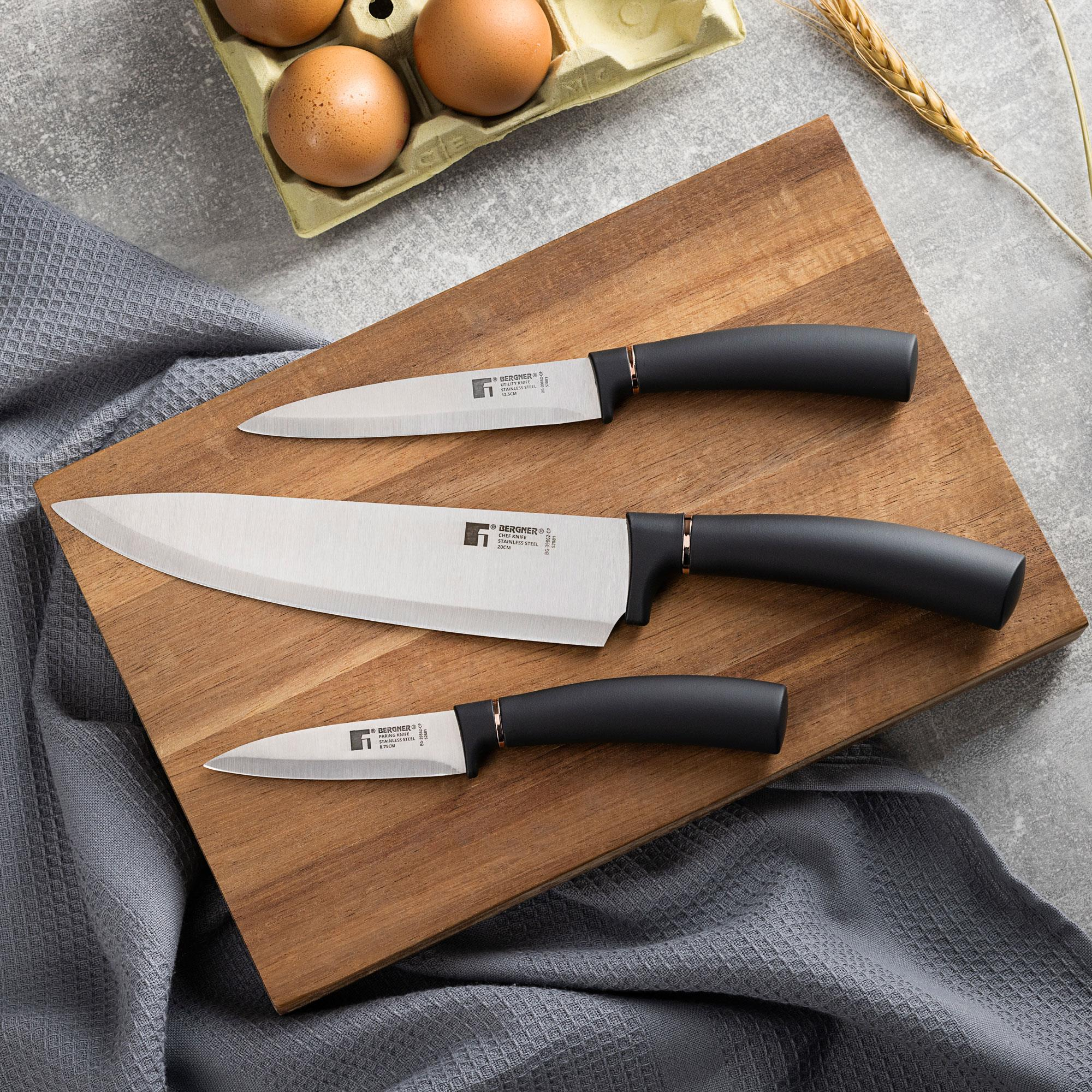 Tres cuchillos en una tabla de madera, con huevos y un paño en el fondo.