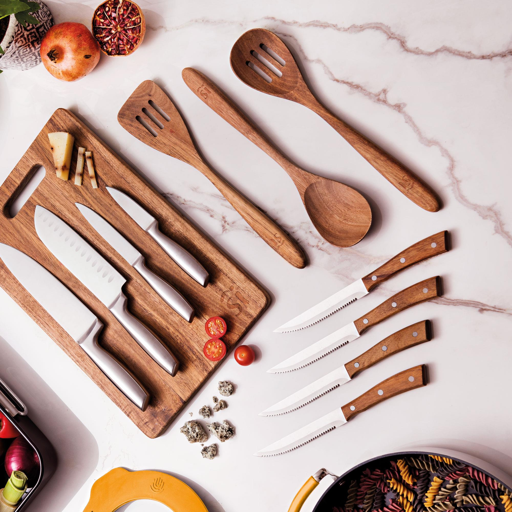 Utensilios de cocina de madera, cuchillos e ingredientes sobre mármol. Incluye queso, granada y pasta.