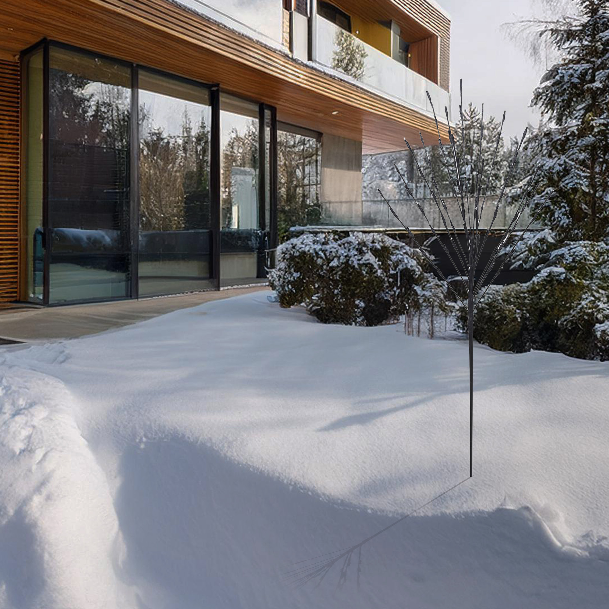 Una casa moderna con césped cubierto de nieve. Una planta decorativa en la nieve. Árboles al fondo.
