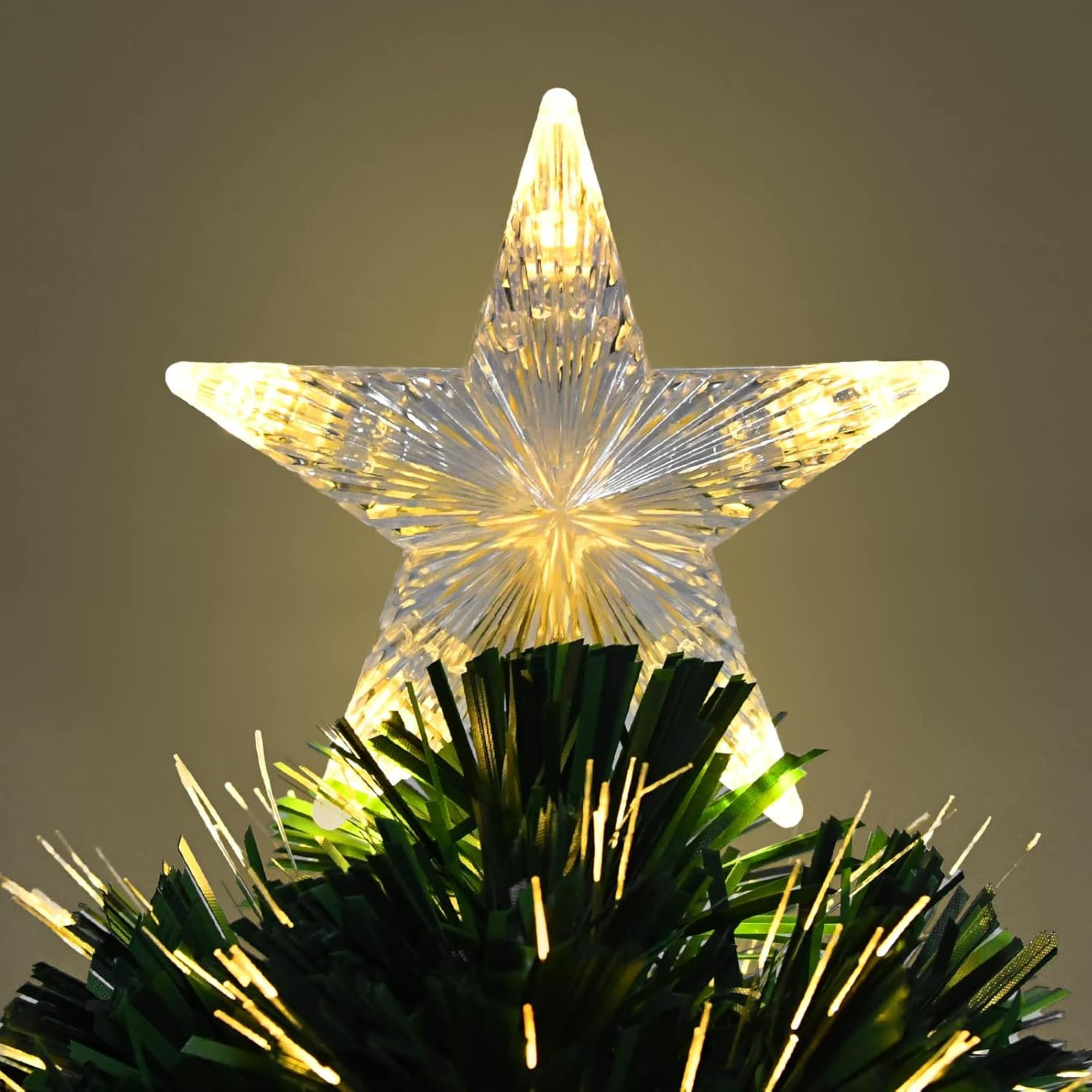 Una estrella iluminada en la cima de un árbol de Navidad. La estrella es translúcida y brillante. Ramas verdes debajo.