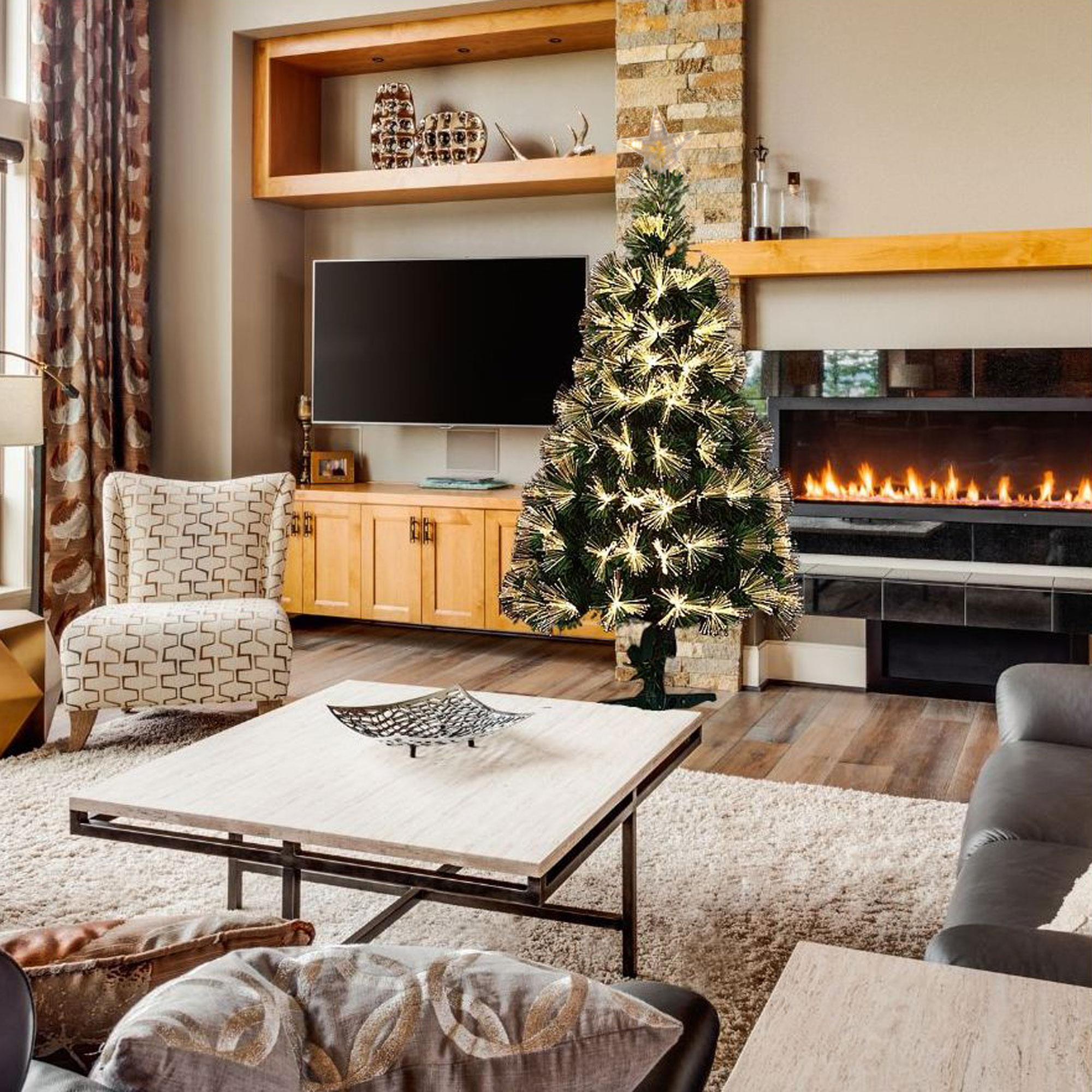 Escena de sala de estar con árbol de Navidad encendido, chimenea, sofá, silla y mesa de centro.