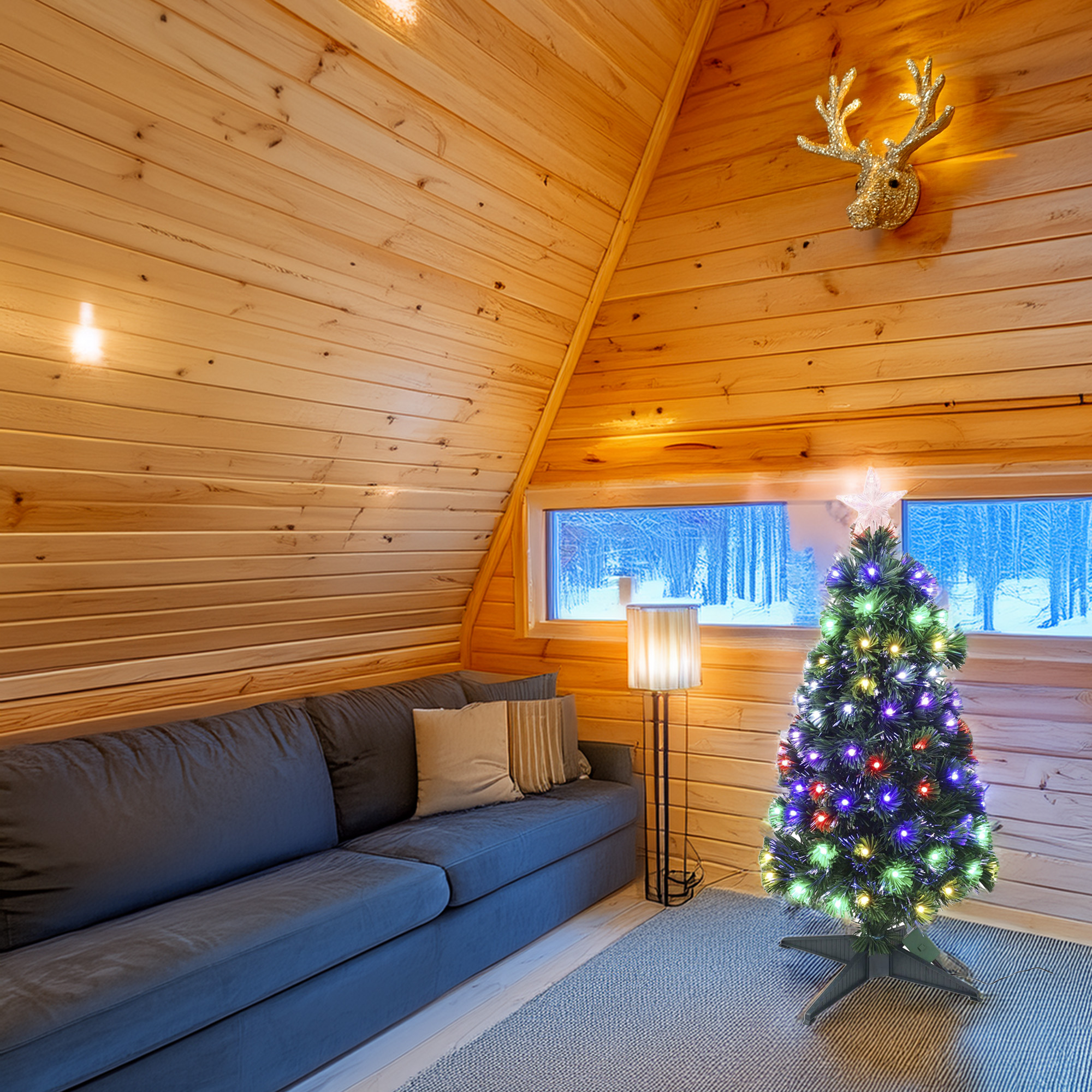 Interior de cabaña con sofá, árbol de Navidad y cabeza de ciervo dorada en pared de madera.