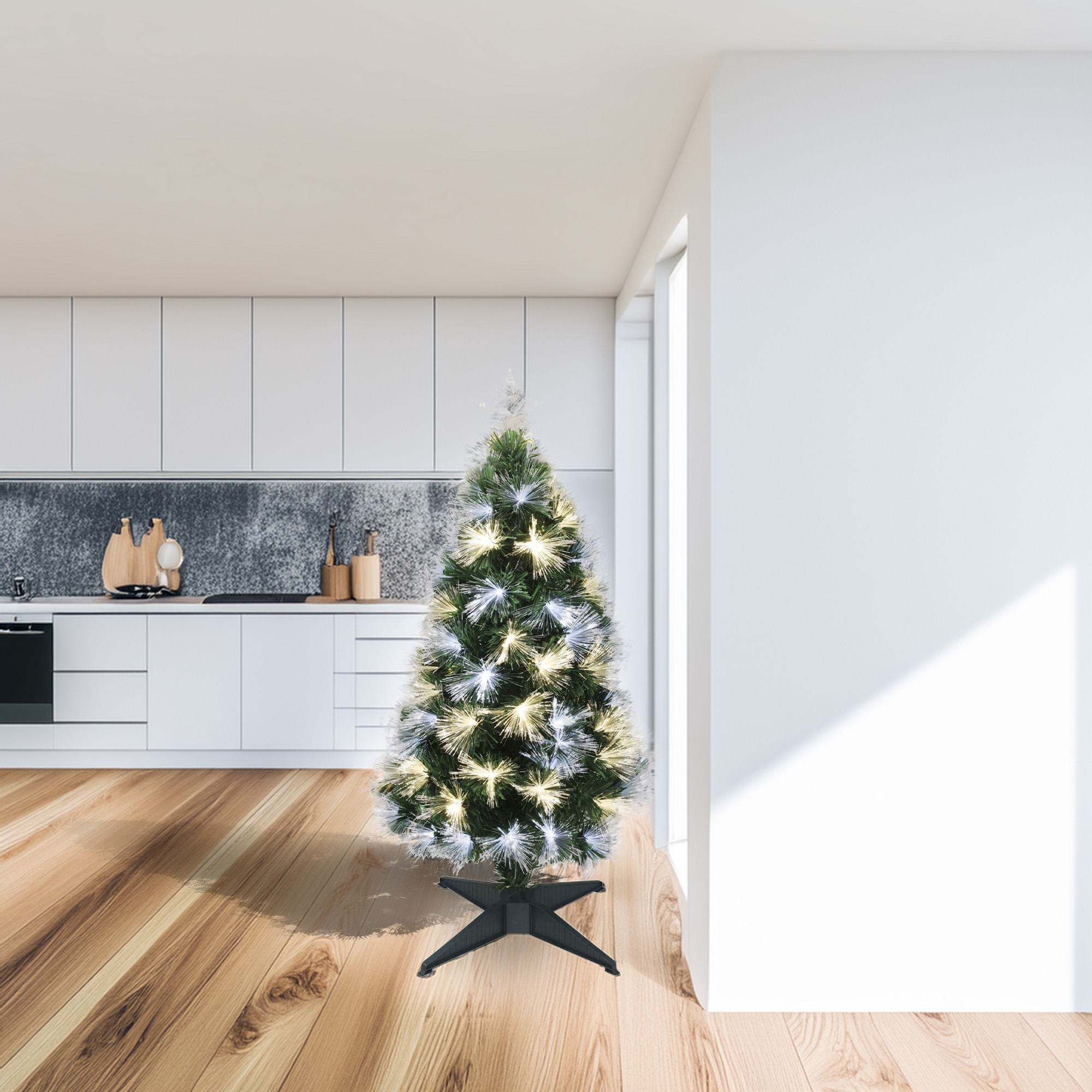Un árbol de Navidad iluminado se encuentra en una cocina. La cocina tiene gabinetes blancos, piso de madera y un salpicadero oscuro.