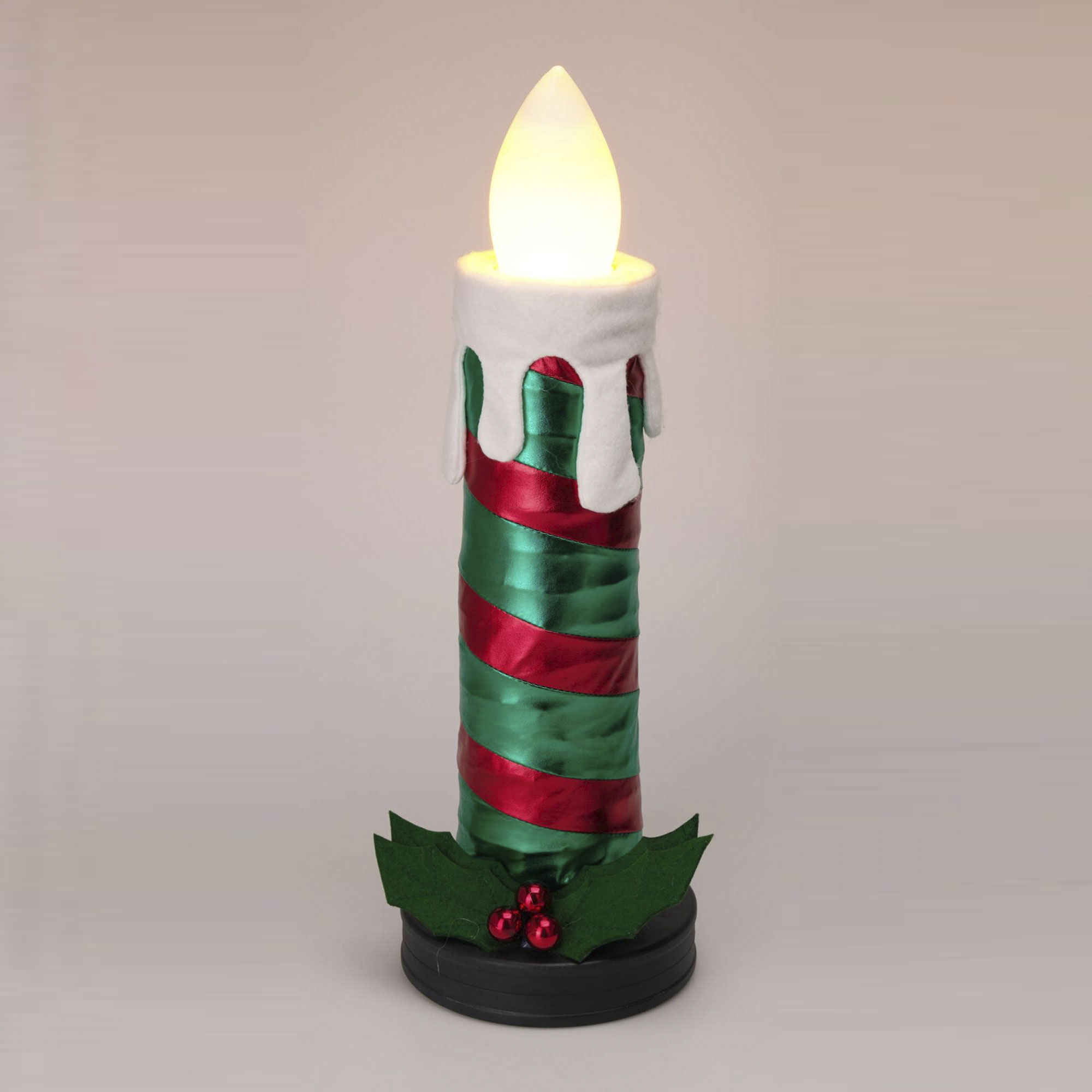 Una vela navideña decorativa. Tiene una parte superior blanca con una llama brillante, cinta verde y roja y hojas de acebo en la base.