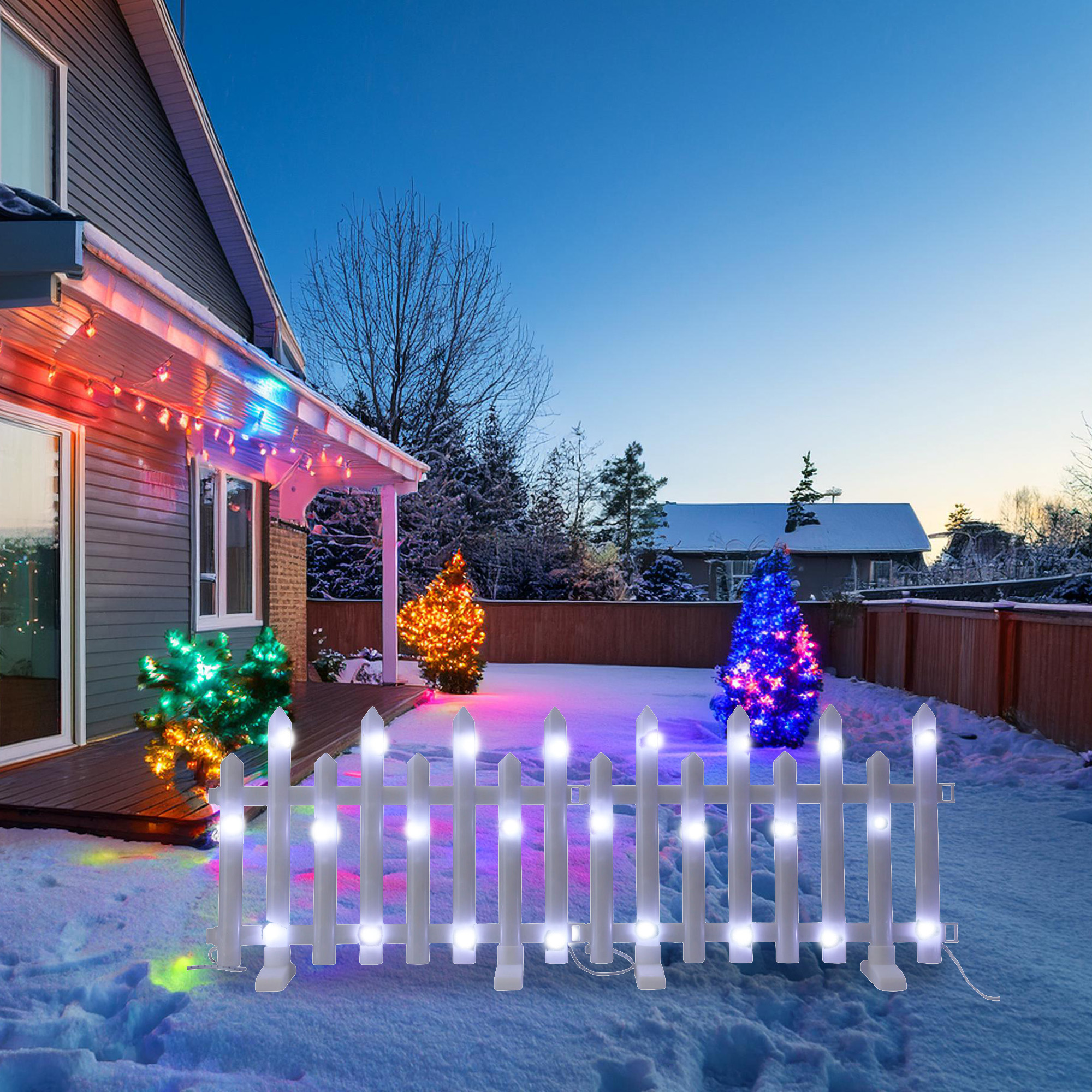 Una casa con luces navideñas, nieve y una valla blanca con luces. Los árboles también están decorados con luces.
