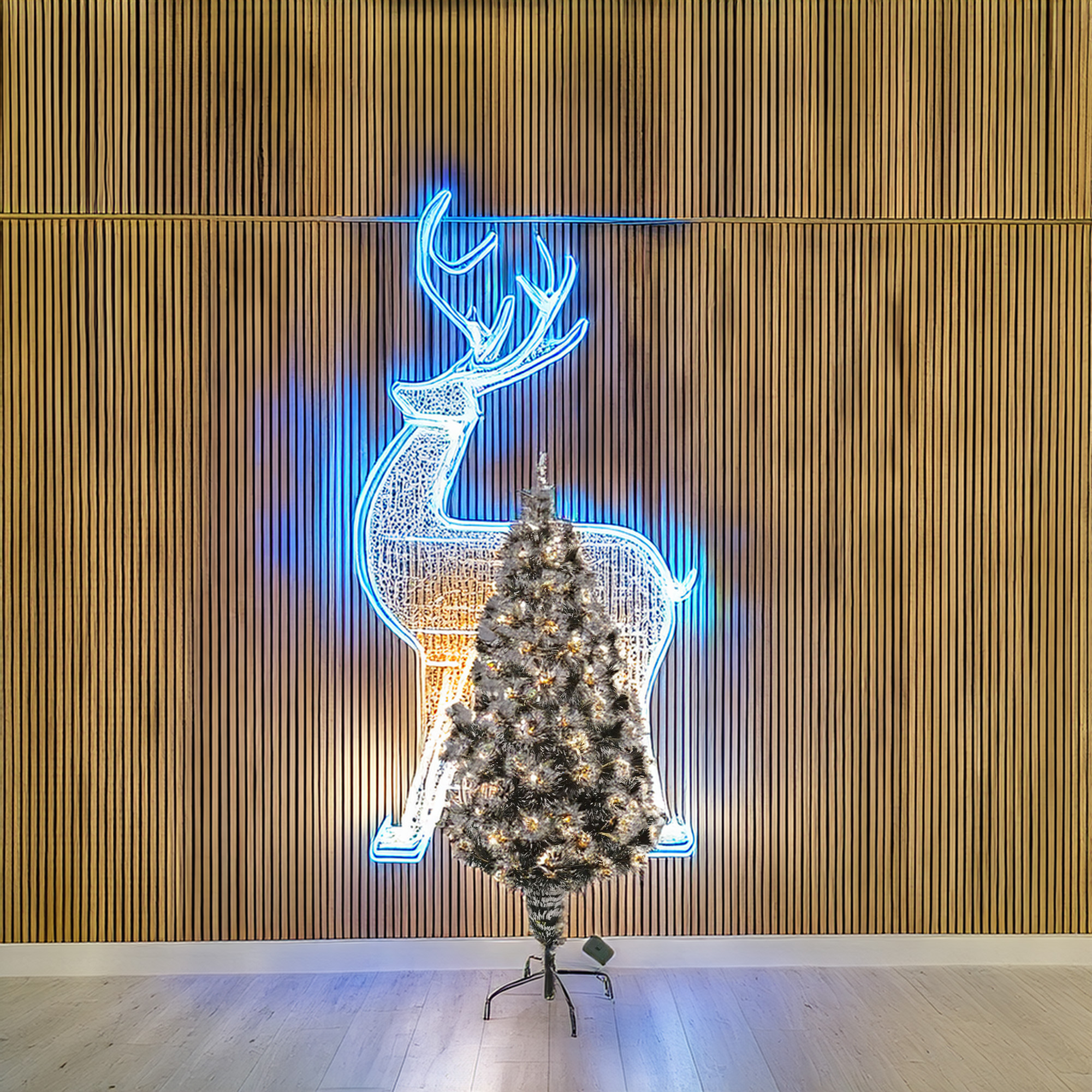 Un árbol de Navidad frente a una pared con un contorno de ciervo de neón. Suelo de madera y paneles de pared.