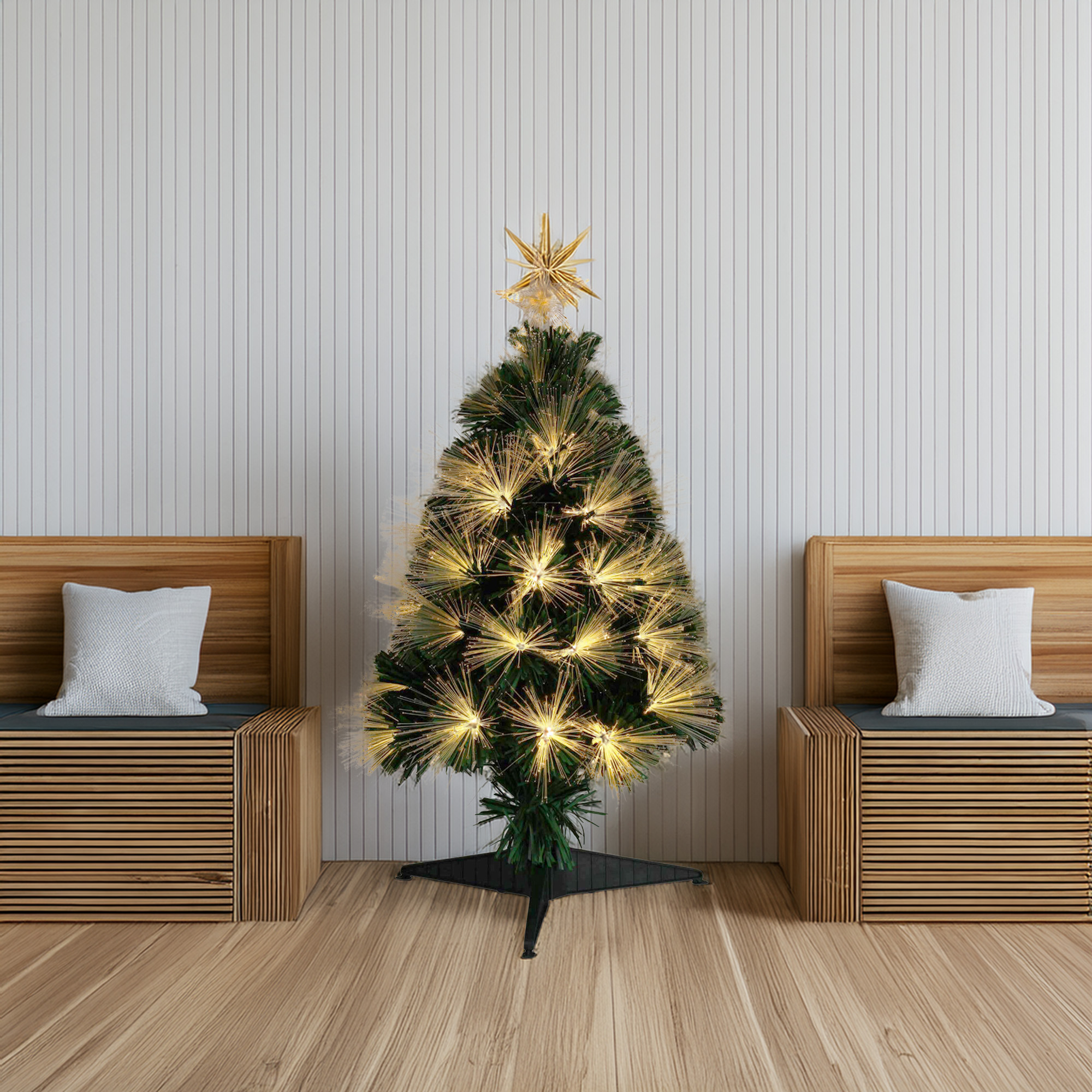 Un árbol de Navidad iluminado con estrella en la cima, entre dos bancos de madera con almohadas, contra una pared blanca.