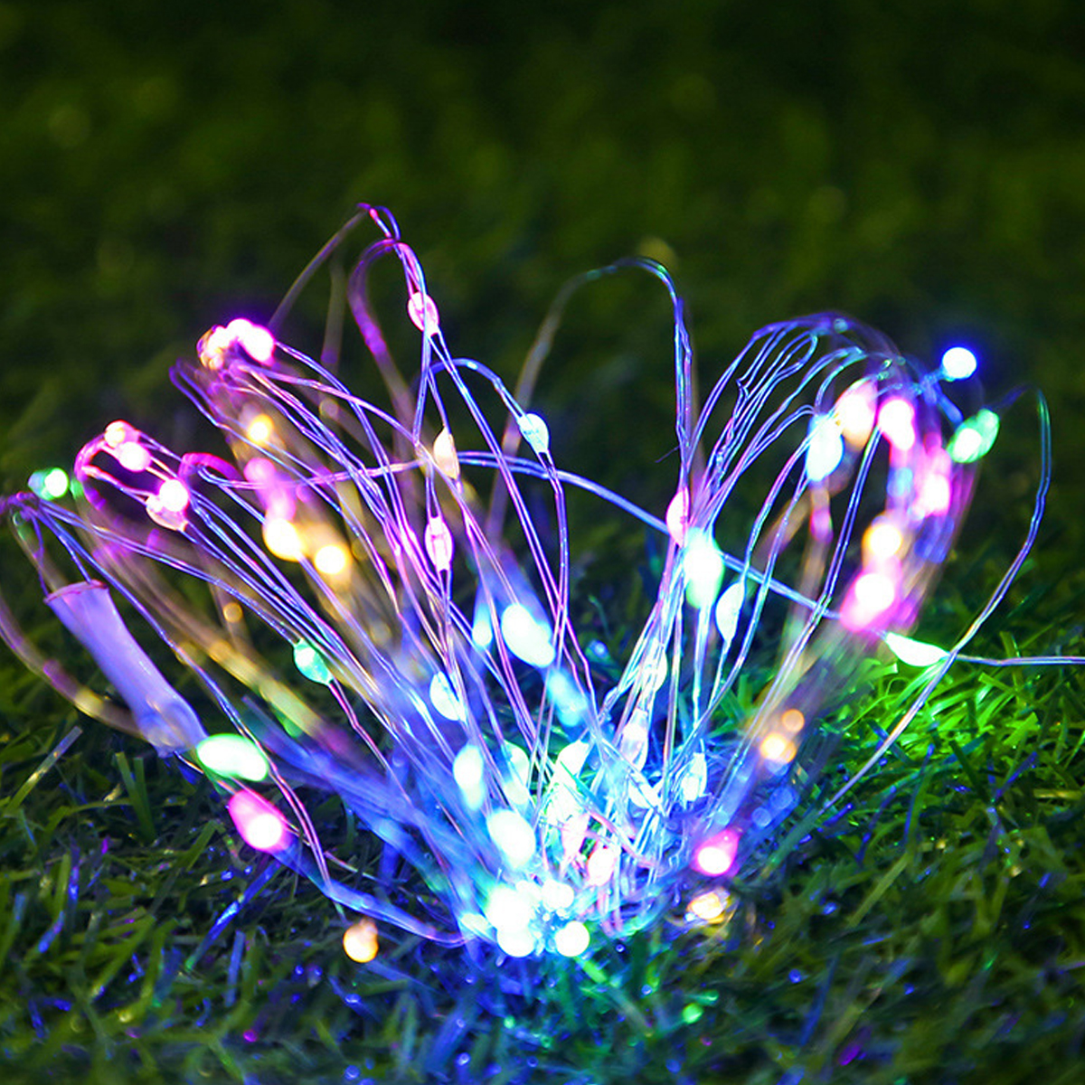 Luci a stringa con LED colorati su erba verde. Le luci hanno sfumature blu, rosa e gialle.