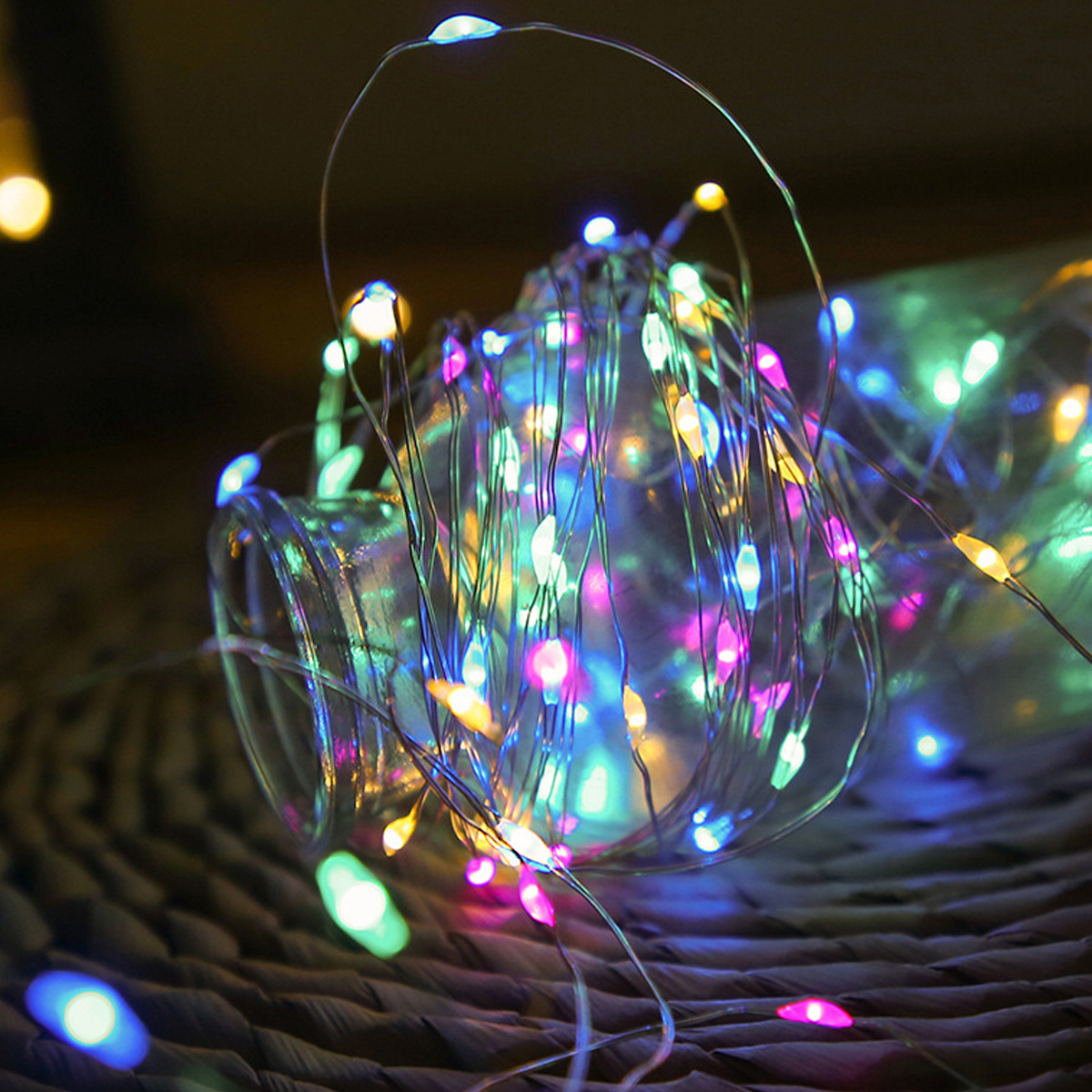 Un barattolo di vetro pieno di luci a stringa multicolore si trova su una superficie tessuta. Le luci sono di vari colori, tra cui blu e rosa.