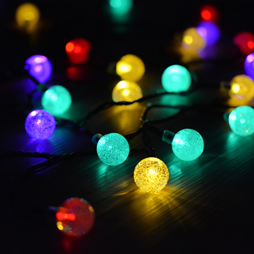 Fili di luci a globo colorate e luminose su una superficie scura. Vari colori come giallo, verde, viola e rosso.