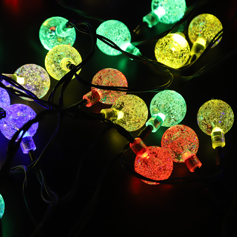 Filo di luci a globo colorate e luminose. I colori includono verde, giallo, rosso e viola. Sfondo scuro.